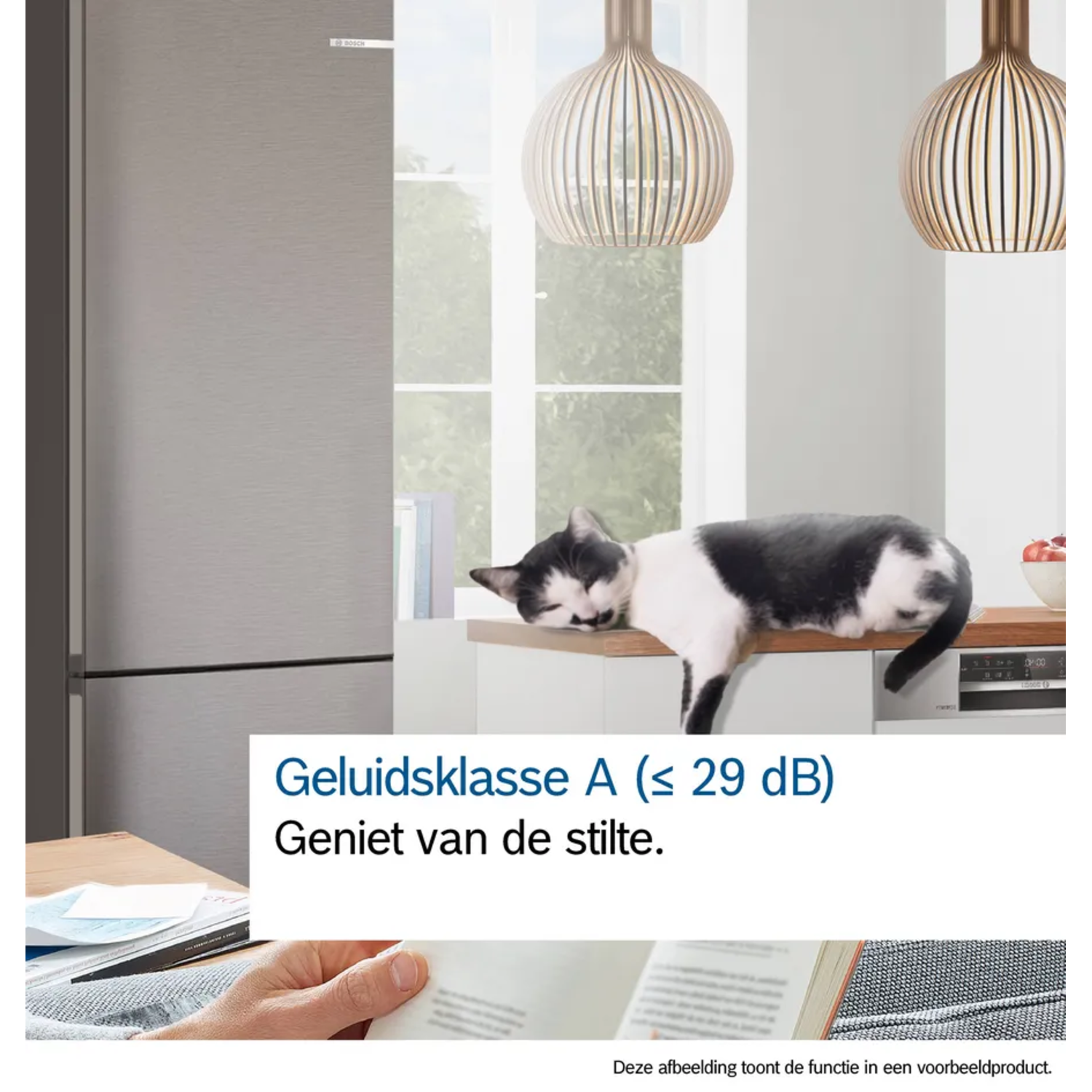 A black and white cat lies on a counter. A refrigerator is on the left. Two lights hang from the ceiling.