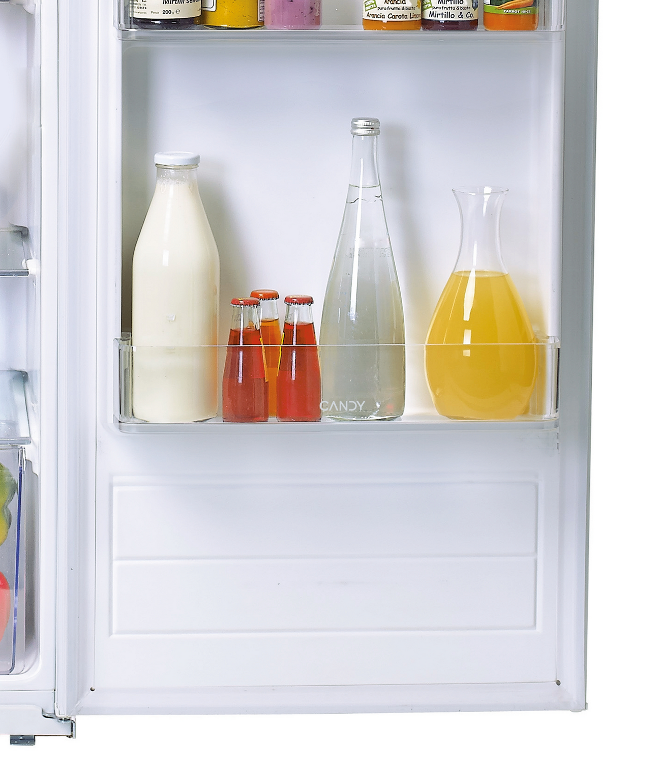 Dentro de un refrigerador: Botella de leche, pequeñas botellas coloridas, botella de agua y jugo en una jarra. Estante superior con frascos.