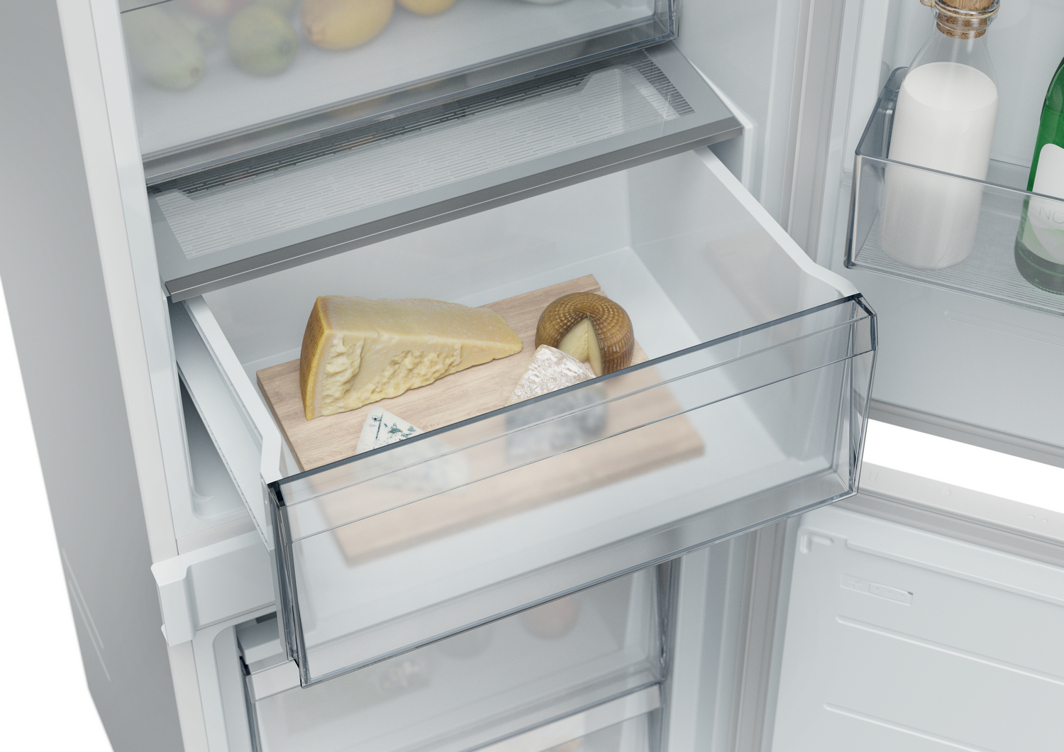 Cajón de refrigerador con varios quesos en una tabla de madera. Otros estantes tienen frutas, botellas y una vela.