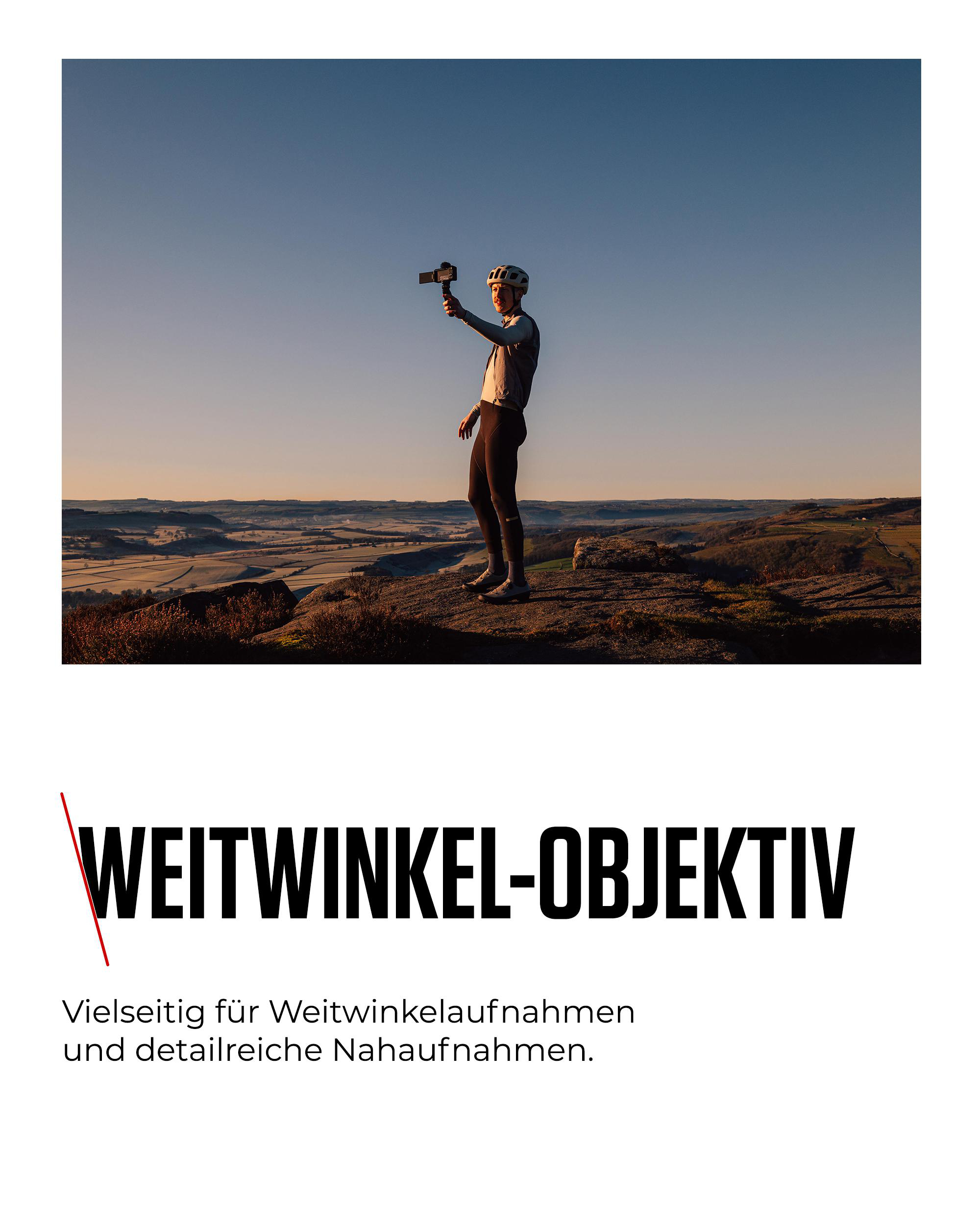 Ein Radfahrer hält eine Kamera auf einem Berg. Der Hintergrund zeigt eine Landschaft unter blauem Himmel.