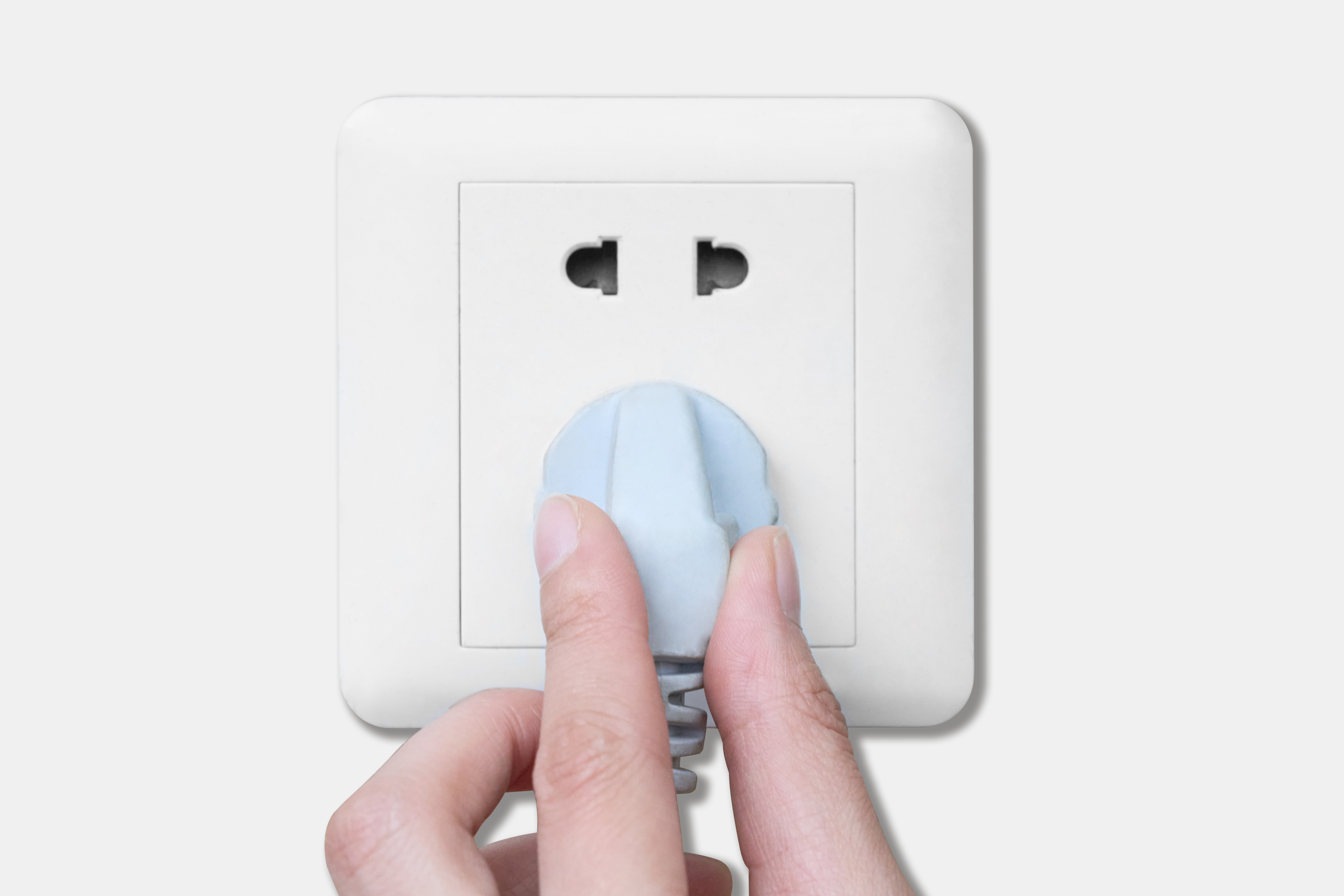 Eine Hand steckt einen blauen Stecker in eine weiße Steckdose. Die Steckdose befindet sich an einer weißen Wand.