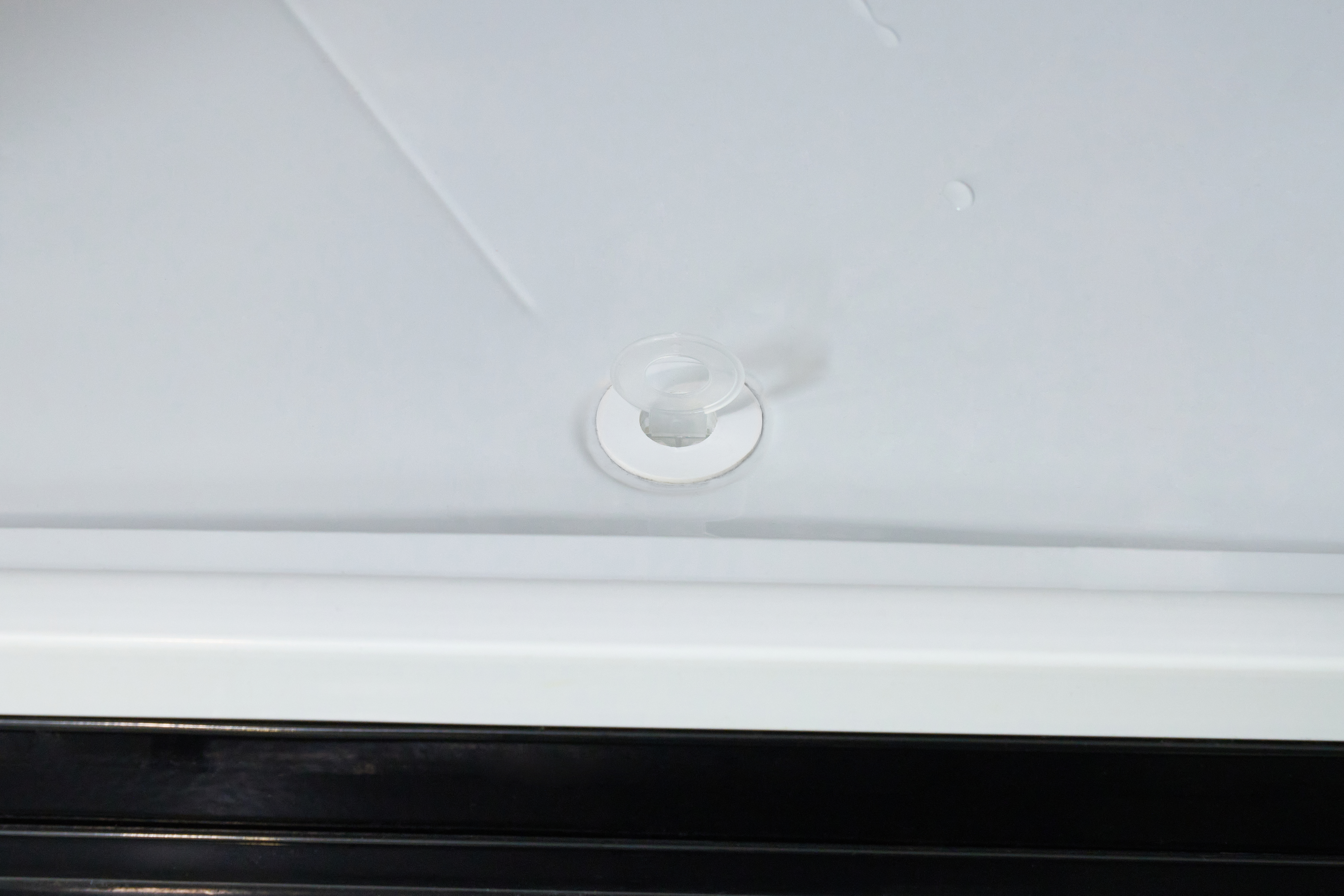 Nahaufnahme einer weißen Oberfläche mit einem kleinen, durchsichtigen Kunststofffitting. Am Boden eine schwarze Oberfläche.
