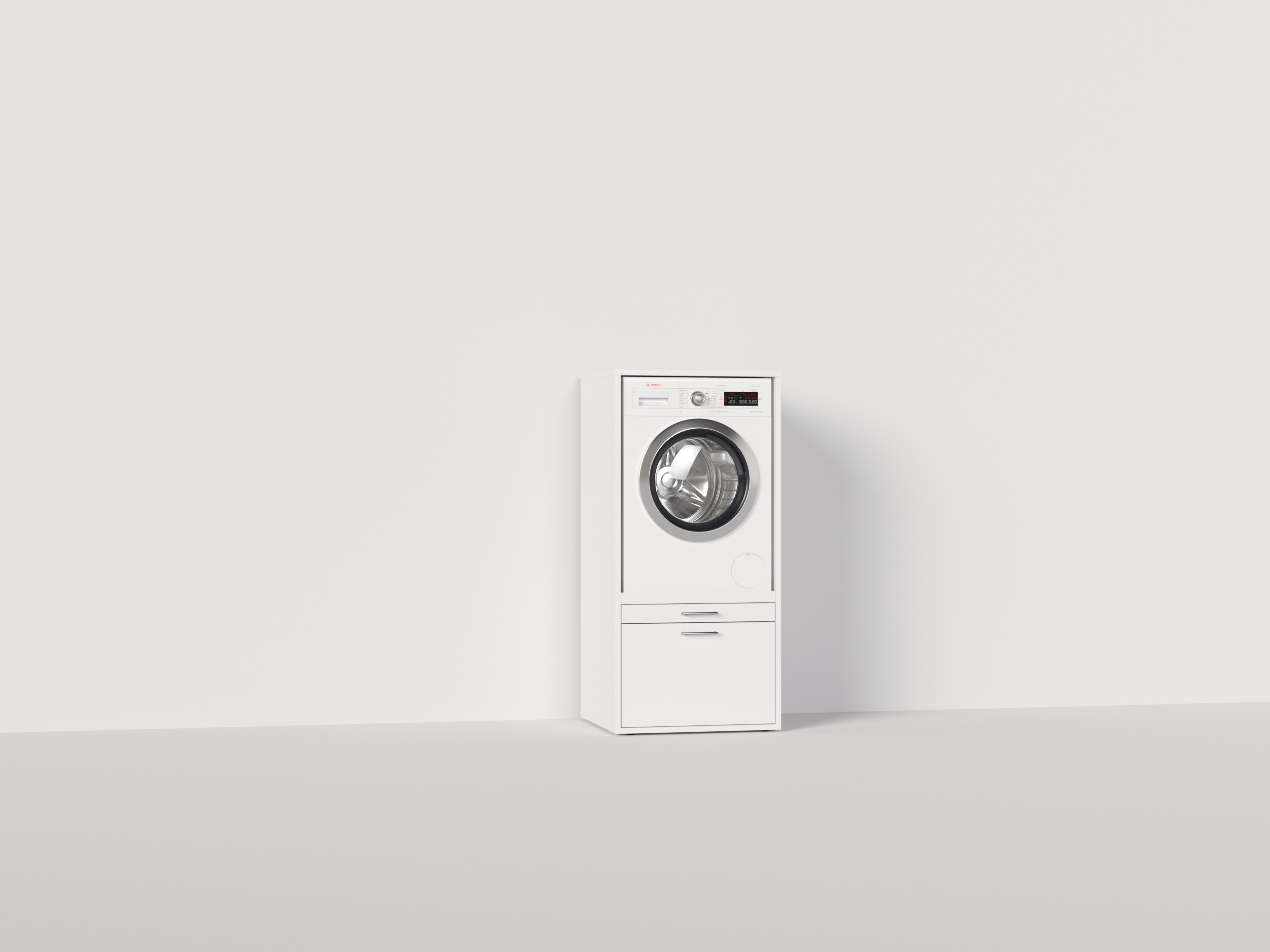 Eine weiße Waschmaschine mit einer Schublade darunter, vor einer weißen Wand und einem weißen Boden.