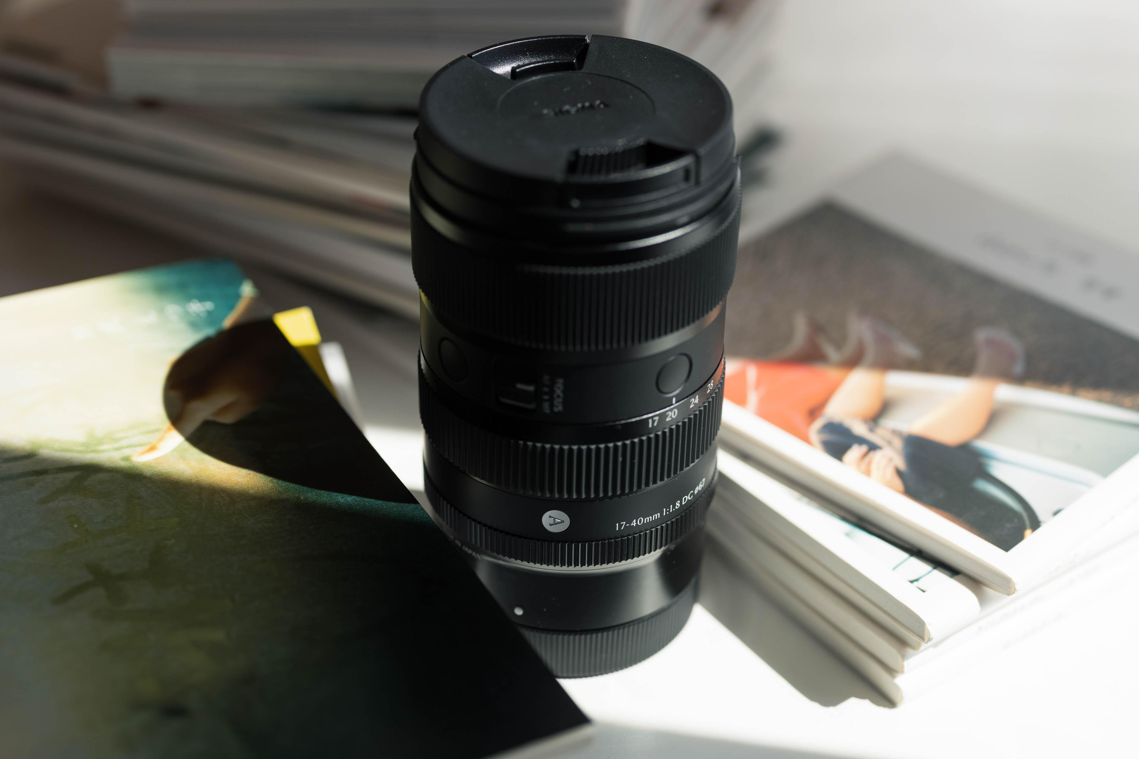 Ein schwarzes Sigma 17-40mm Objektiv liegt auf Büchern. Die Szene ist beleuchtet, mit Licht und Schatten.