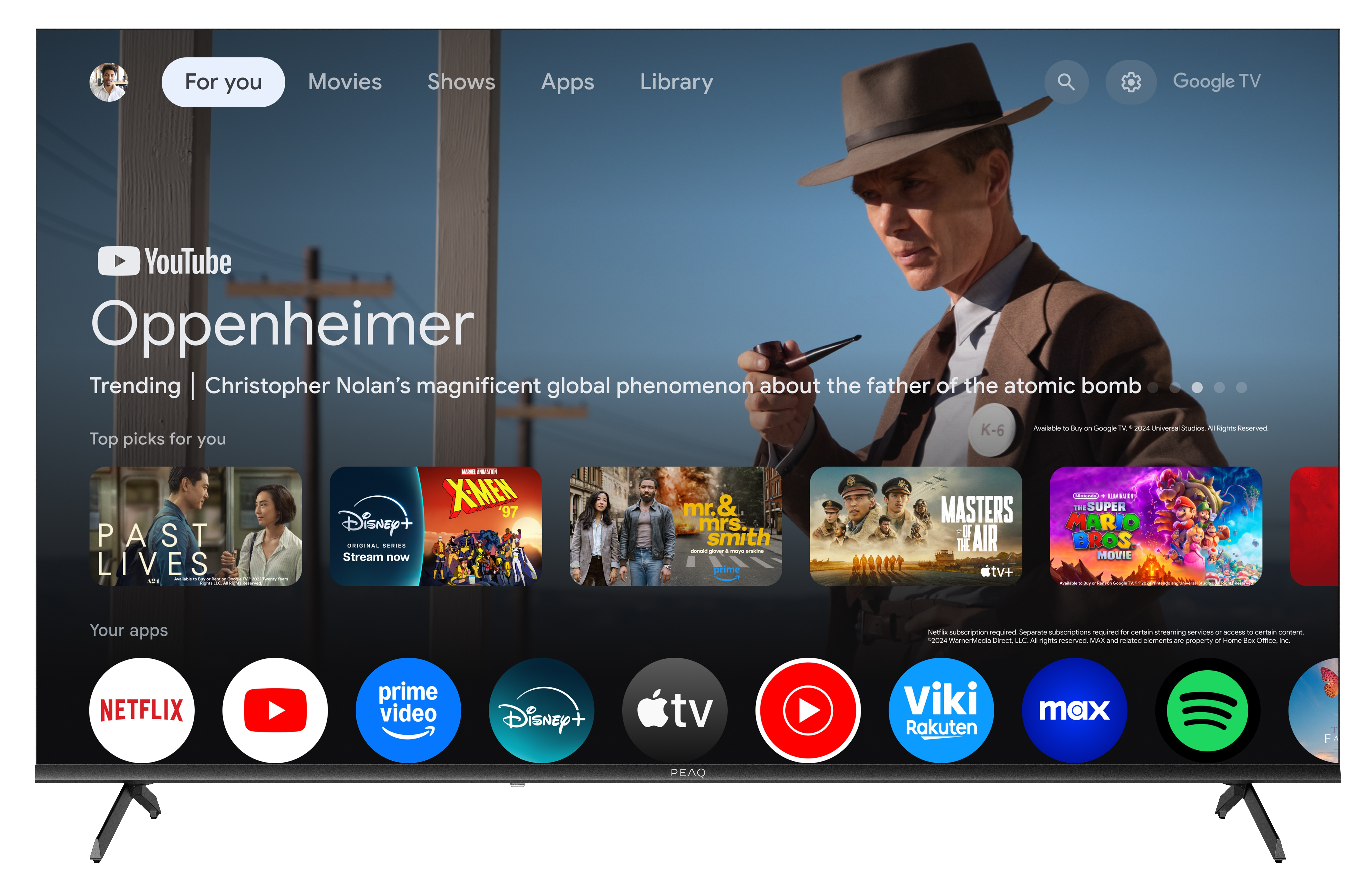 Ekran telewizora wyświetla film z YouTube o Oppenheimerze. Poniżej ikony aplikacji i mężczyzna w kapeluszu w tle.