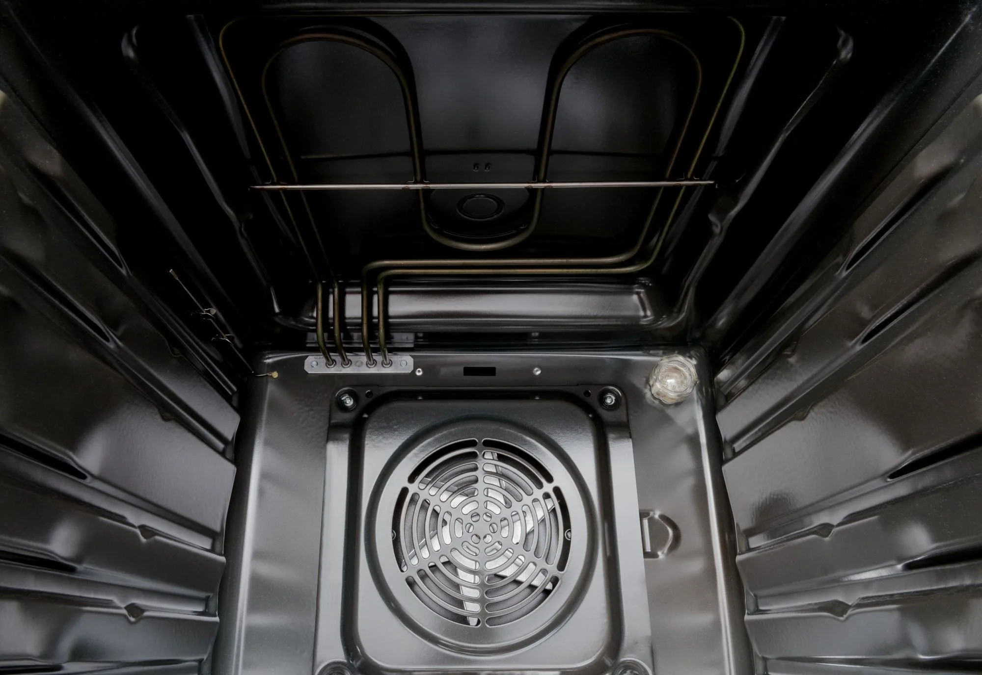 Wnętrze czarnego piekarnika. Widoczne elementy grzejne i wentylator. Wnętrze piekarnika jest błyszczące i odbijające światło.