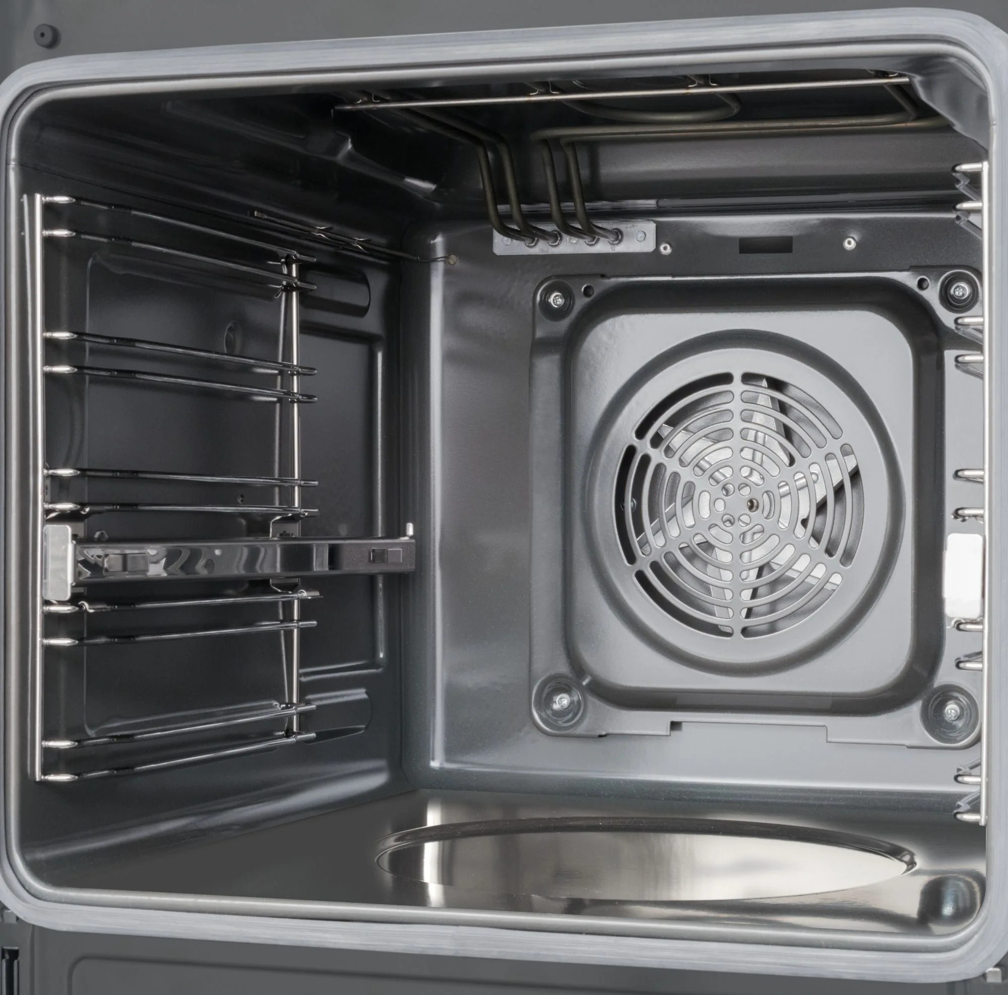 Widok wewnątrz piekarnika. Metalowe ruszty, elementy grzejne i wentylator są widoczne w szarym wnętrzu.