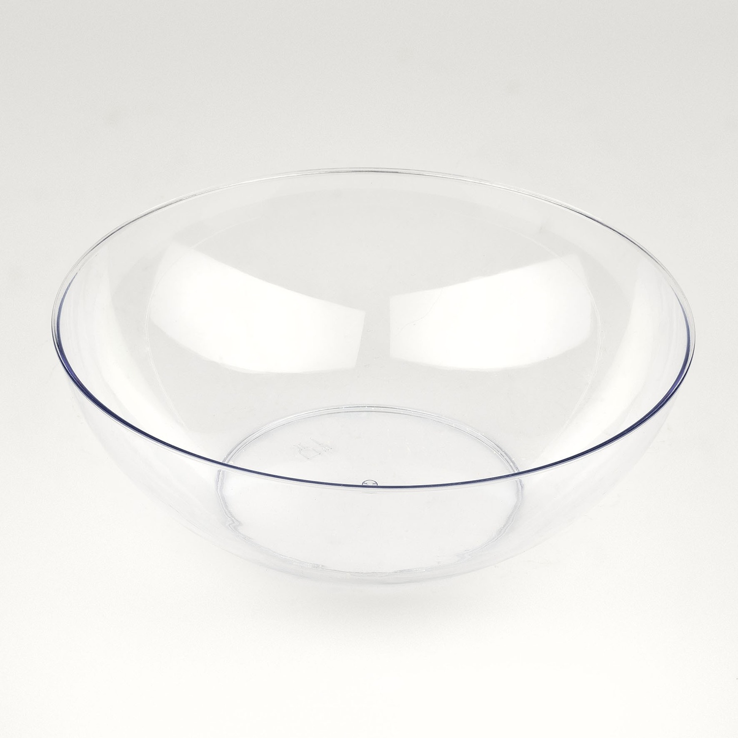 Una ciotola di plastica trasparente e chiara è su una superficie bianca. La ciotola è vuota e riflette la luce circostante.