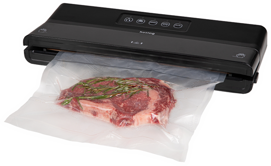Egy fekete vákuumos tömítőgép, amely egy steak-et rozmaringgal lezár egy átlátszó műanyag zacskóban. Fehér háttér.