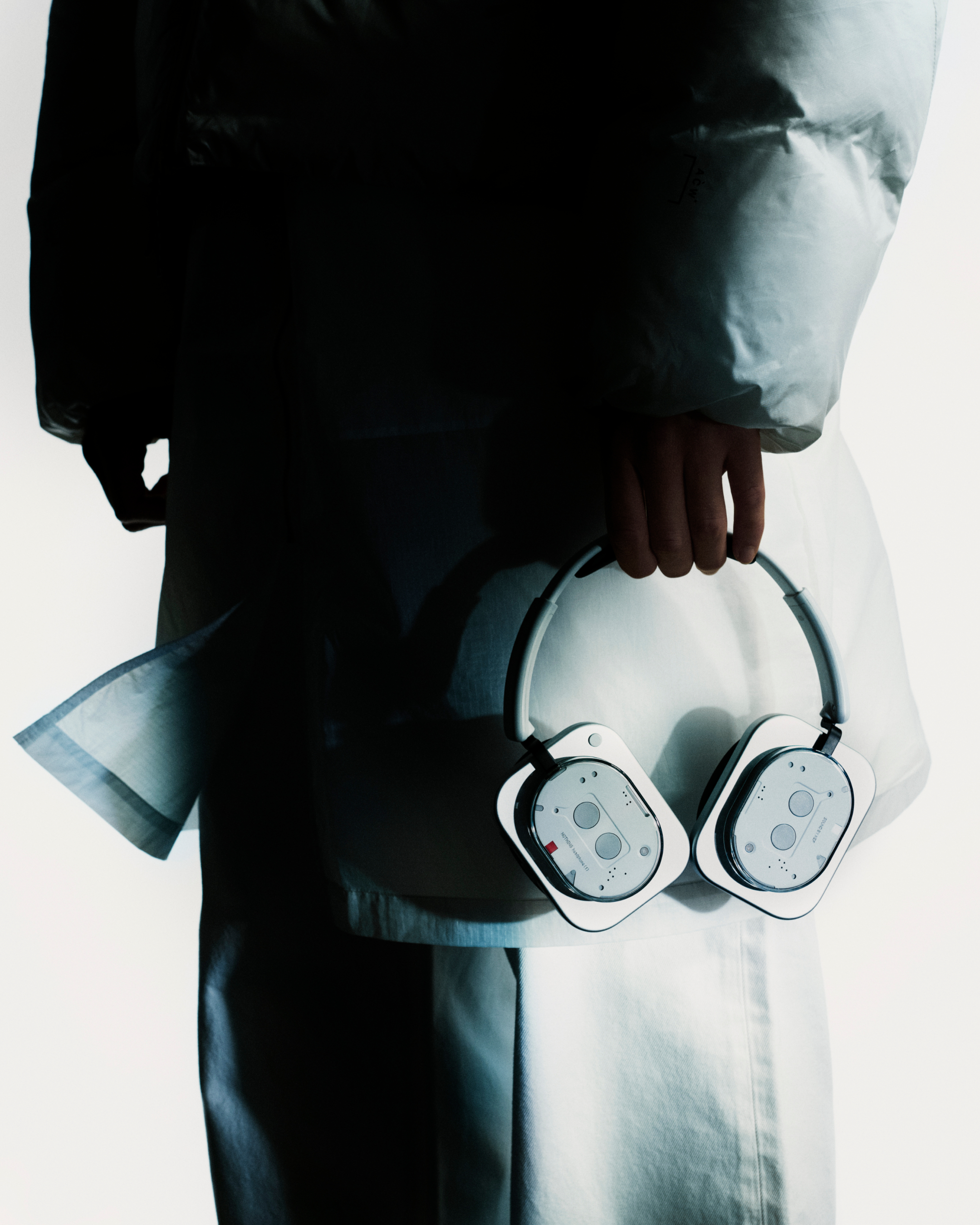 Person hält weiße Kopfhörer. Die Person trägt eine weiße Jacke. Der Hintergrund ist weiß.