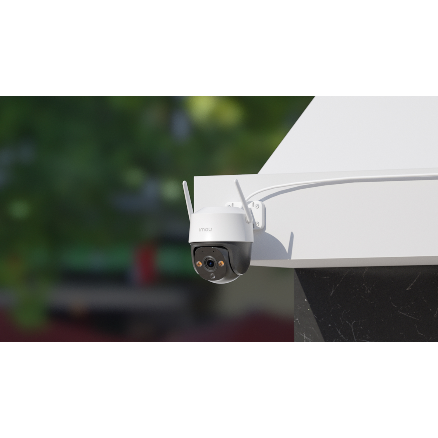 A white and black security camera with antennas is mounted on a white structure. Green foliage is blurred in the background.