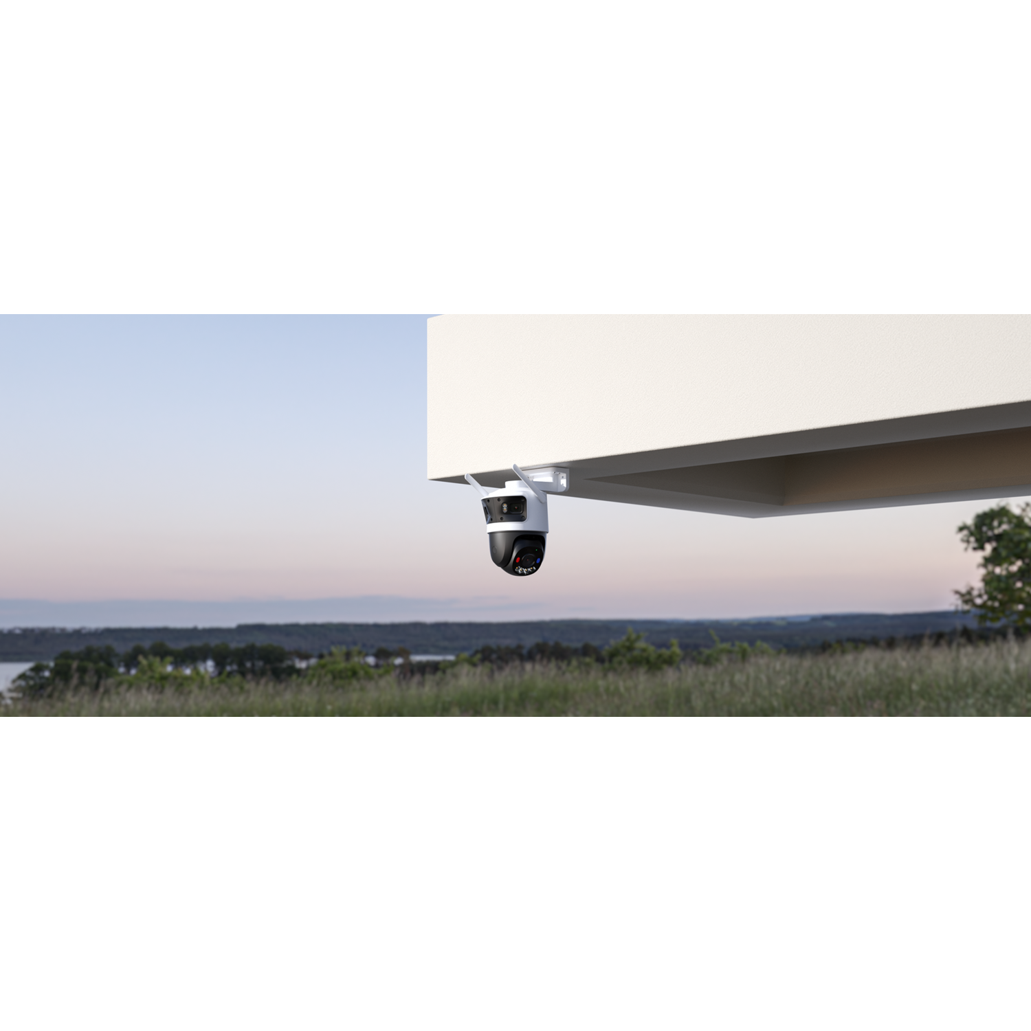 A security camera is mounted under a white structure. The background shows a landscape with grass, trees, and a body of water.