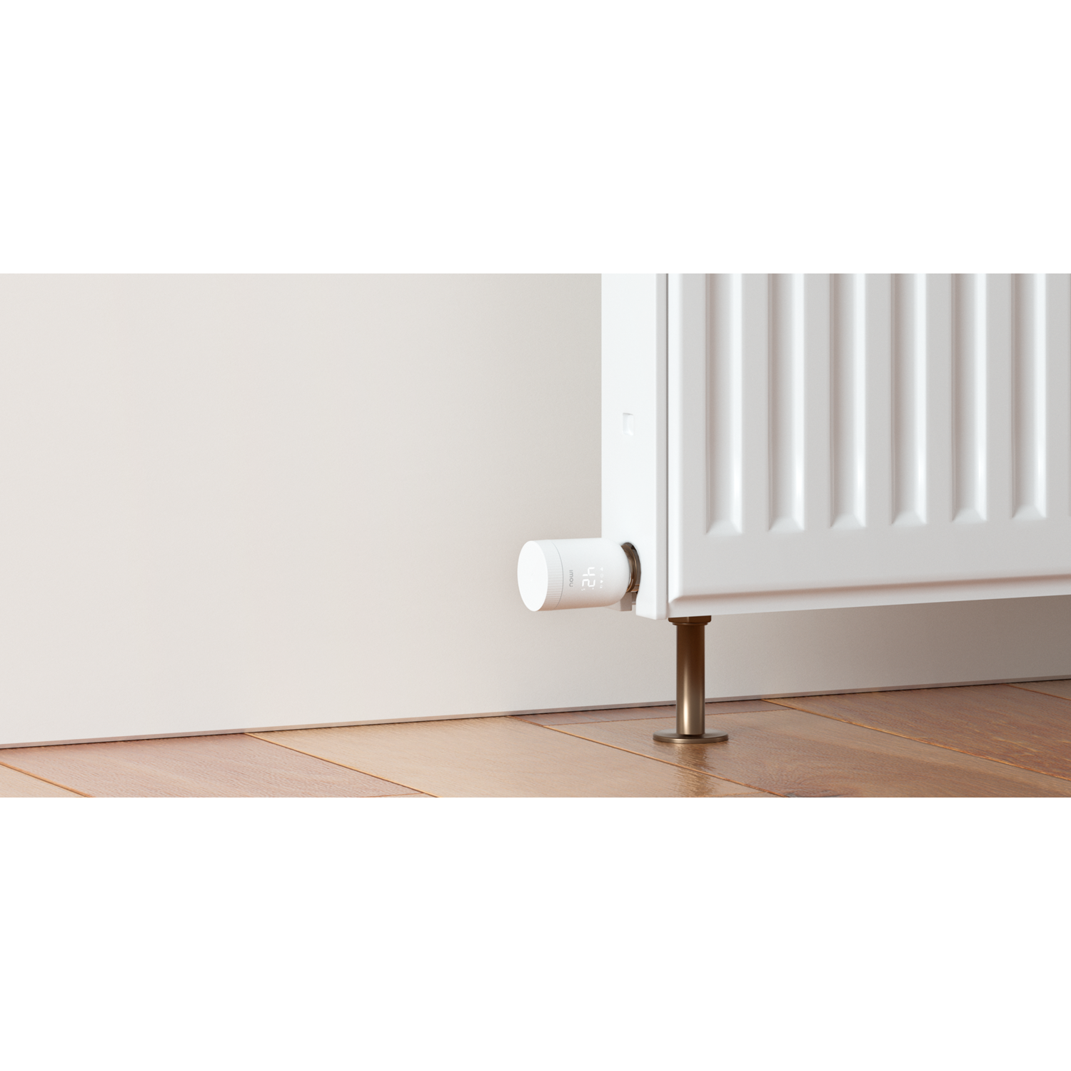 A white radiator with a smart thermostat attached. The thermostat displays the temperature. The radiator stands on golden legs, on wooden floor.