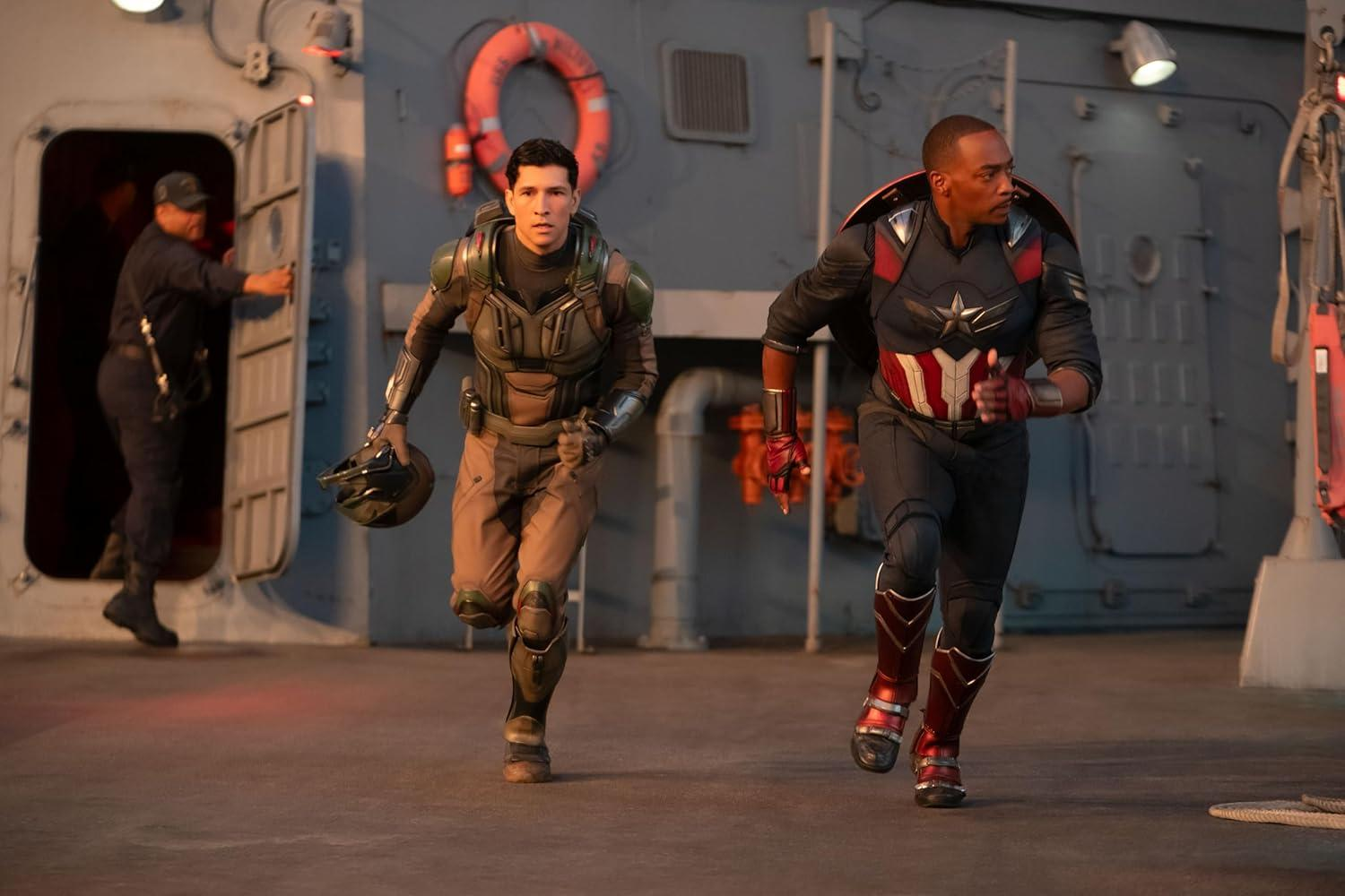 Zwei Männer in Kostümen rennen auf einem Schiffsdeck. Einer ist Captain America. Ein anderer Mann hält einen Helm.