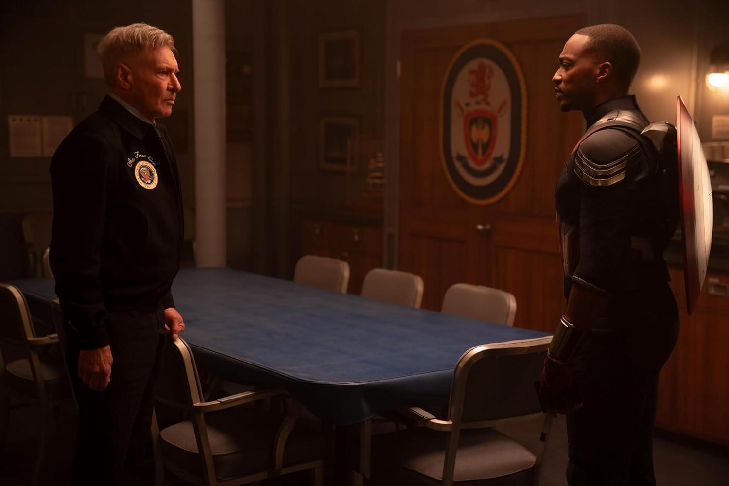 Zwei Männer stehen sich in einem Raum gegenüber. Einer trägt eine Jacke mit Abzeichen, der andere einen Captain America-Anzug.