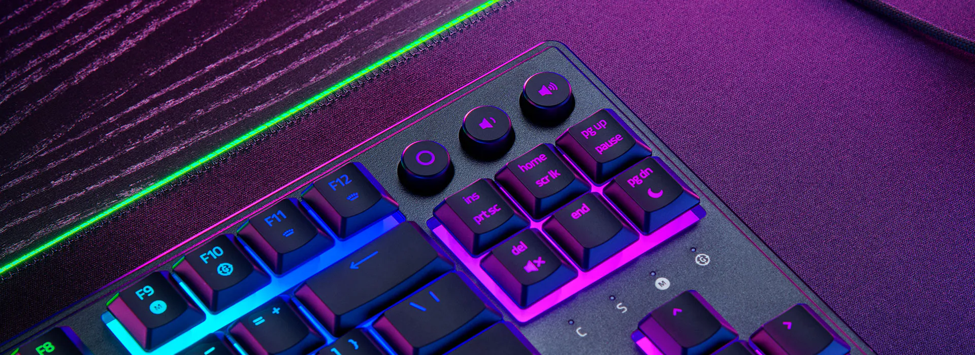 Közelkép egy gamer billentyűzetről, világító gombokkal. A billentyűzet fekete alapon lila és kék fénnyel világít.