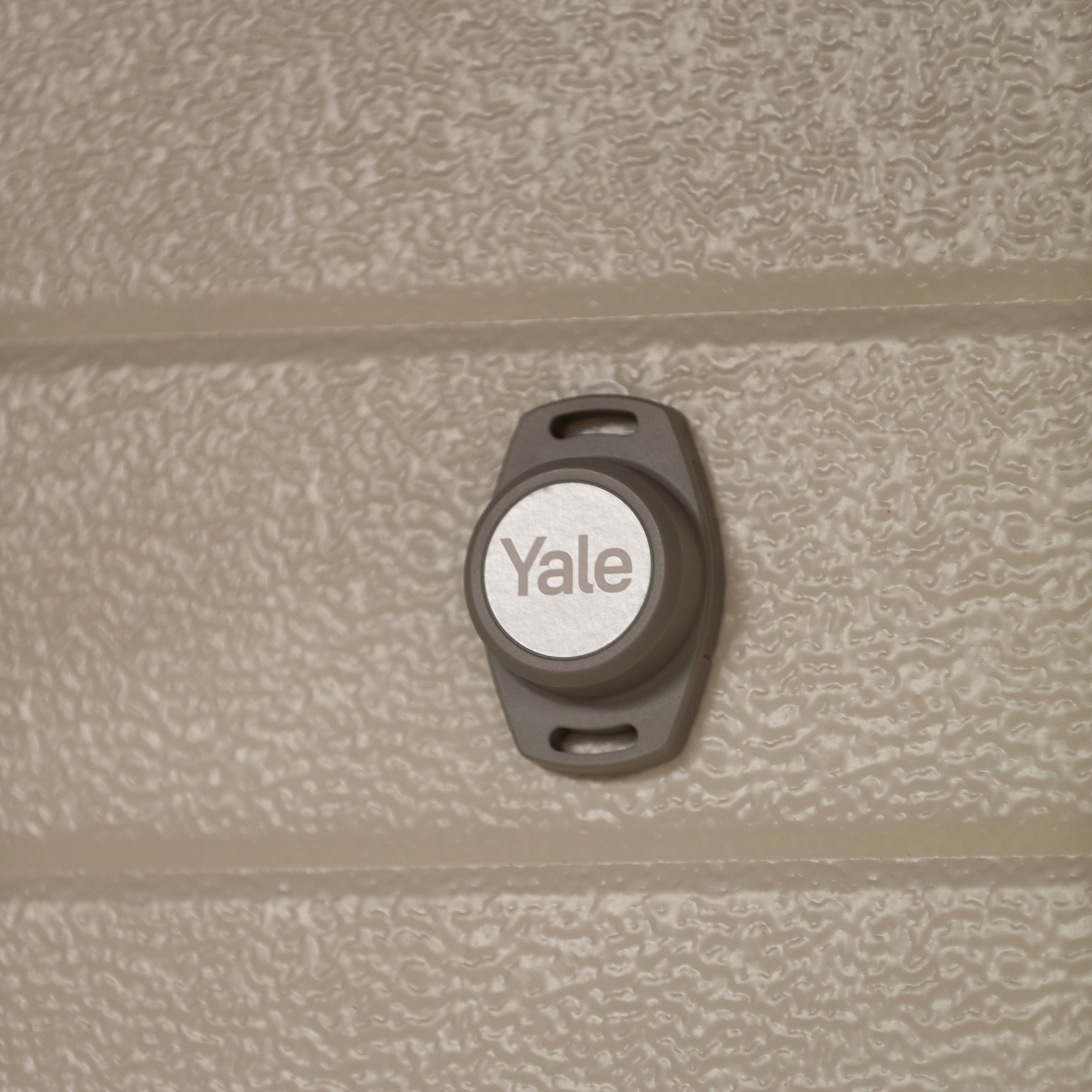 Ein graues Yale Smart Lock ist auf einer strukturierten, beigefarbenen Oberfläche montiert.