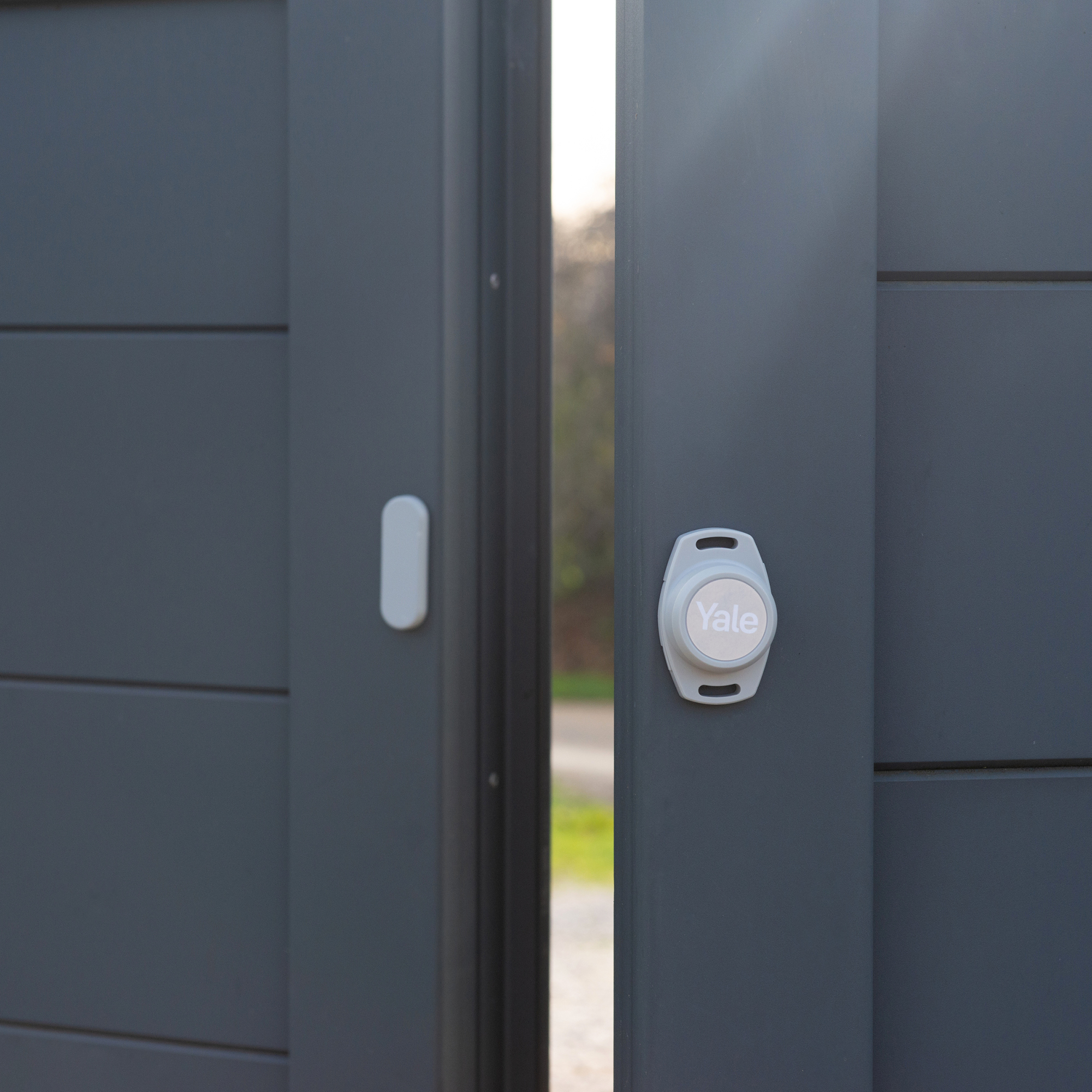 Graues Tor mit Yale Smart Lock. Das Tor ist leicht geöffnet und gibt einen Blick nach draußen frei.