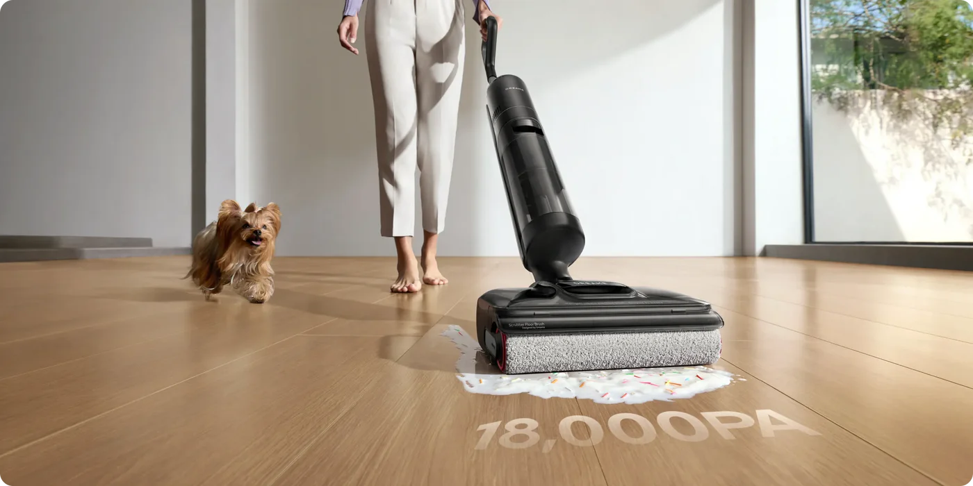 Egy nő fekete porszívót használ fapadlón. Egy kutya elfut. Tej és cukormáz van a padlón. A padlón 18 000PA felirat látható.