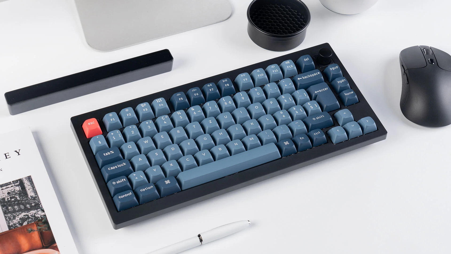 Un clavier mécanique noir avec des touches bleues et une touche échap rouge est sur un bureau blanc, avec une souris.