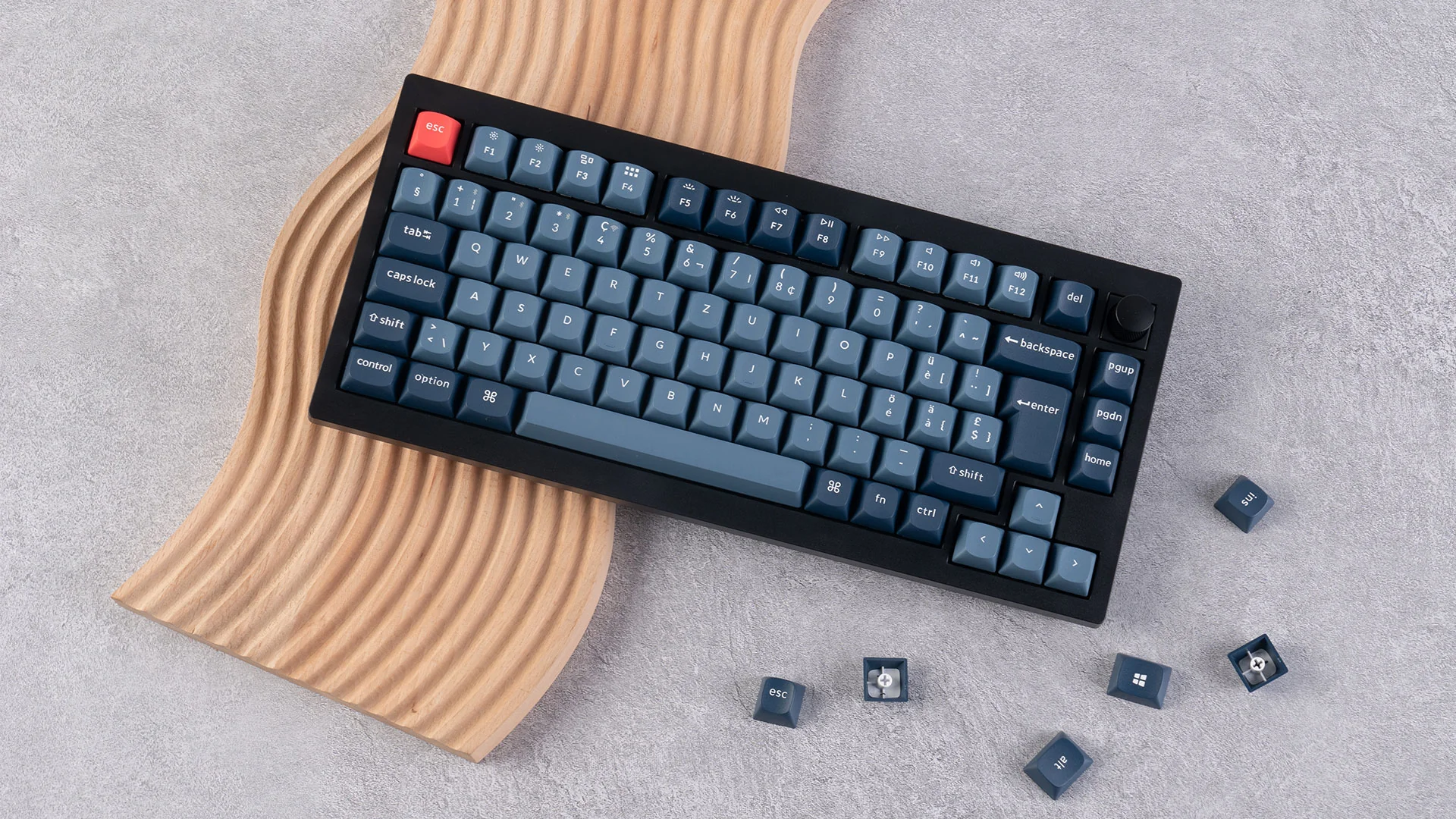 Clavier mécanique noir avec touches bleues, touche échappement rouge, sur surface en bois ondulée. Quelques touches éparpillées.