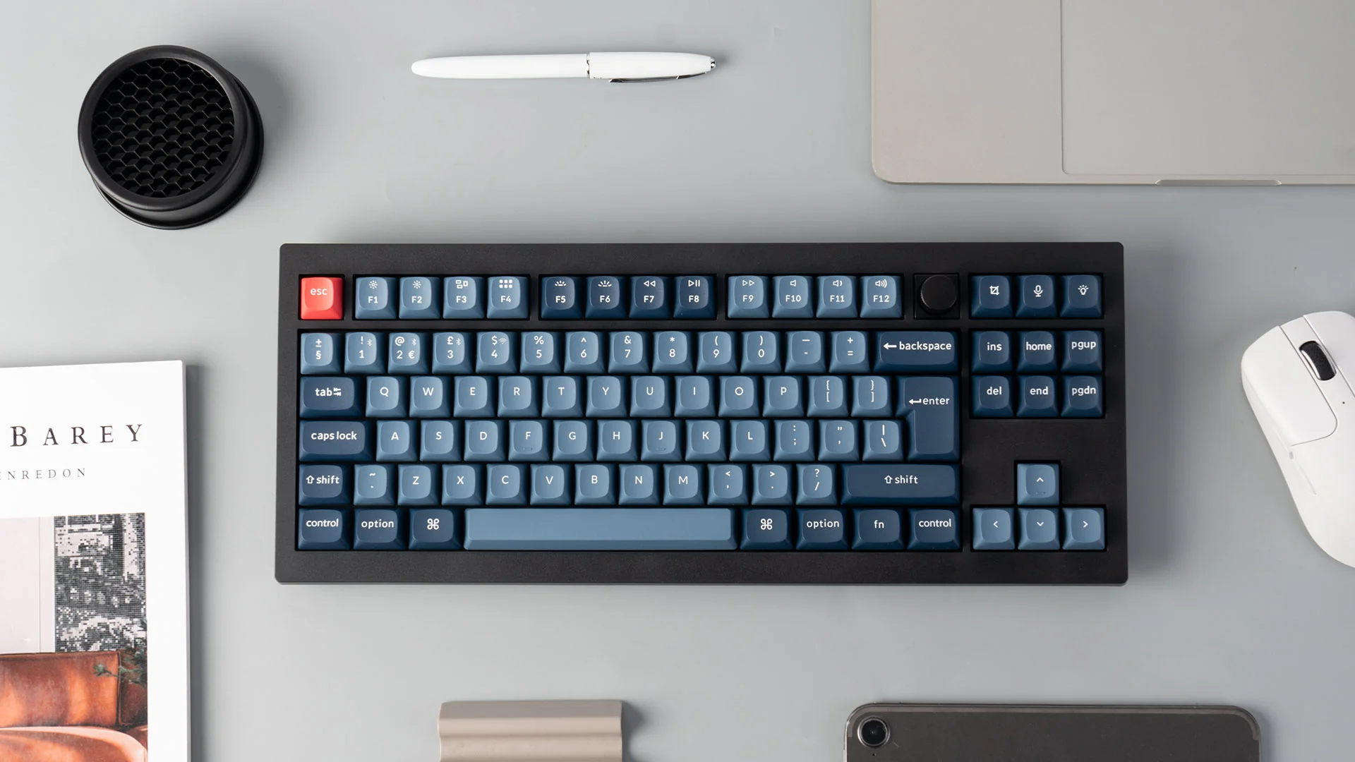 Eine Draufsicht zeigt Tastatur, Maus, Tablet, Stift und Buch auf grauer Oberfläche. Die Tastaturtasten sind blau.