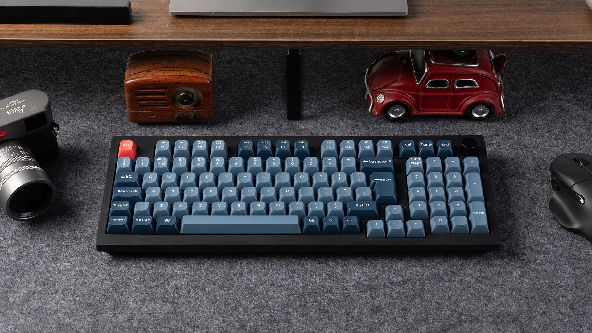 Eine Tastatur mit blauen Tasten liegt auf einer grauen Oberfläche, umgeben von einer Kamera, einem Radio und einem roten Automodell.