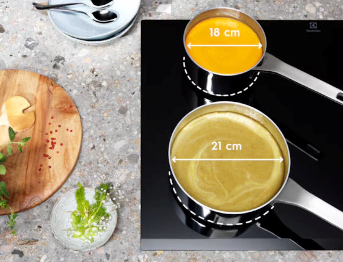 Dwa garnki z zupą na czarnej płycie kuchennej. Jeden garnek ma pomarańczową zupę, drugi żółtą. Obecna jest również drewniana deska, talerze i zioła.