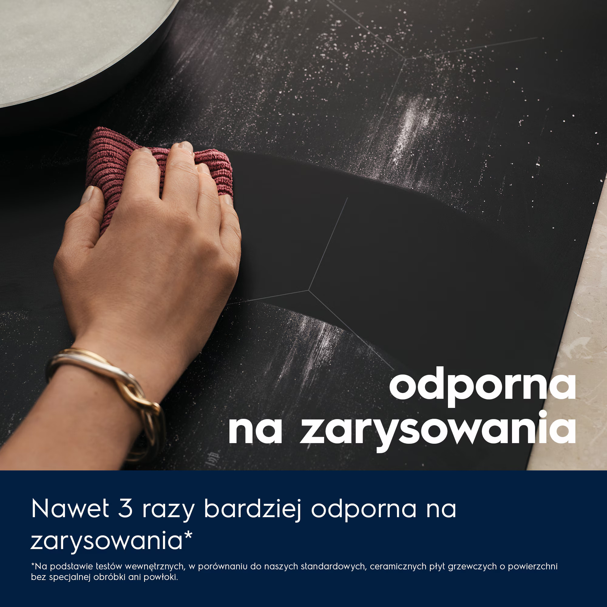 Dłoń wyciera czarną powierzchnię, prawdopodobnie płytę grzewczą, bordową szmatką. Tekst po polsku: odporność na zarysowania.