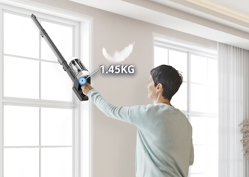 Kobieta używa bezprzewodowego odkurzacza w pobliżu okna. Odkurzacz jest czarny i srebrny.