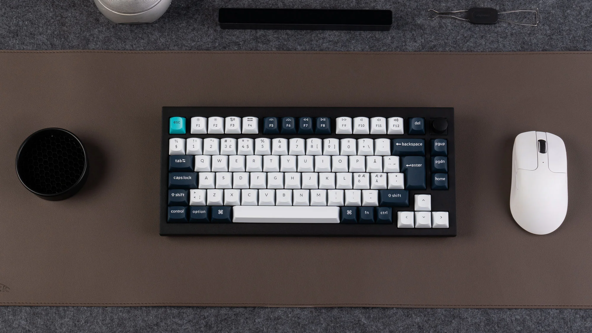 Draufsicht zeigt eine schwarze Tastatur, weiße Maus und anderes Zubehör auf einer braunen Schreibtischunterlage.