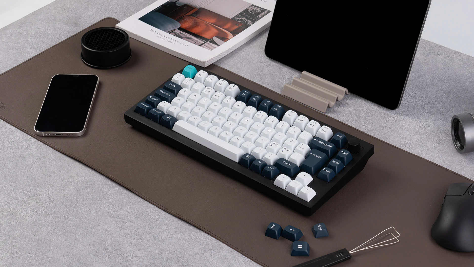 Eine mechanische Tastatur, ein Telefon und ein Tablet auf einem Schreibtisch. Enthält eine Maus, ein Buch und anderes Zubehör. Dunkelbraune Schreibtischunterlage.