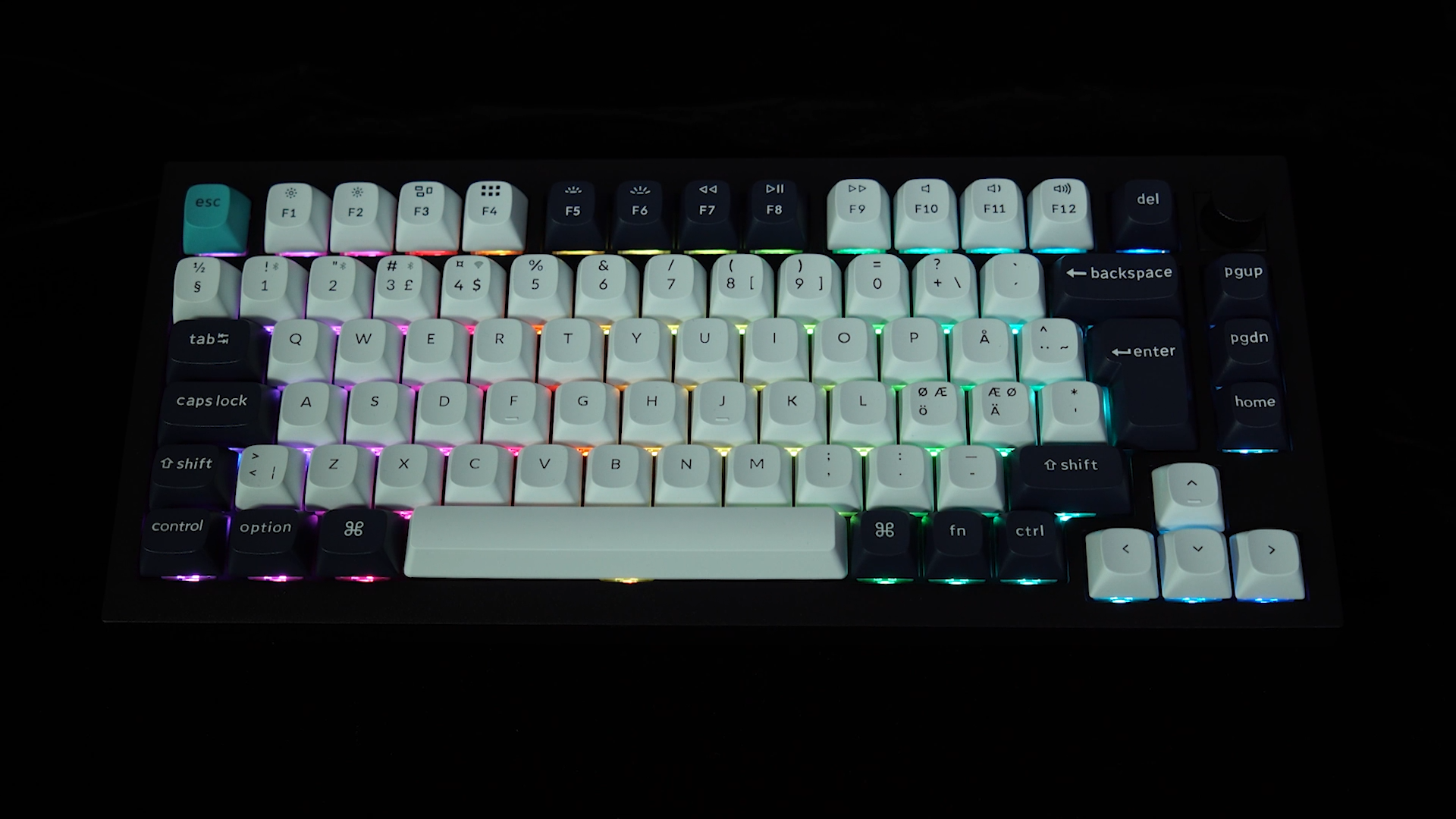 Eine mechanische Tastatur mit weißen Tasten und bunter Hintergrundbeleuchtung liegt auf schwarzem Untergrund. Tasten sind beschriftet.