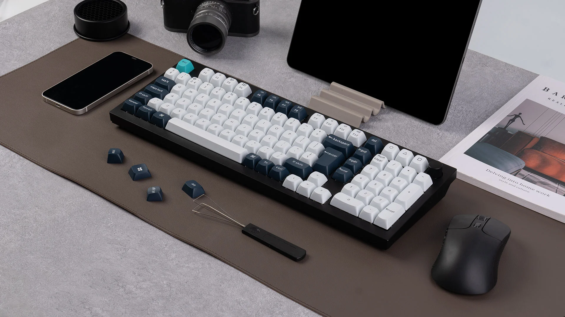 Eine Tastatur mit weißen und blauen Tasten, ein Telefon, eine Kamera, eine Maus und ein Tablet auf einem braunen Pad.