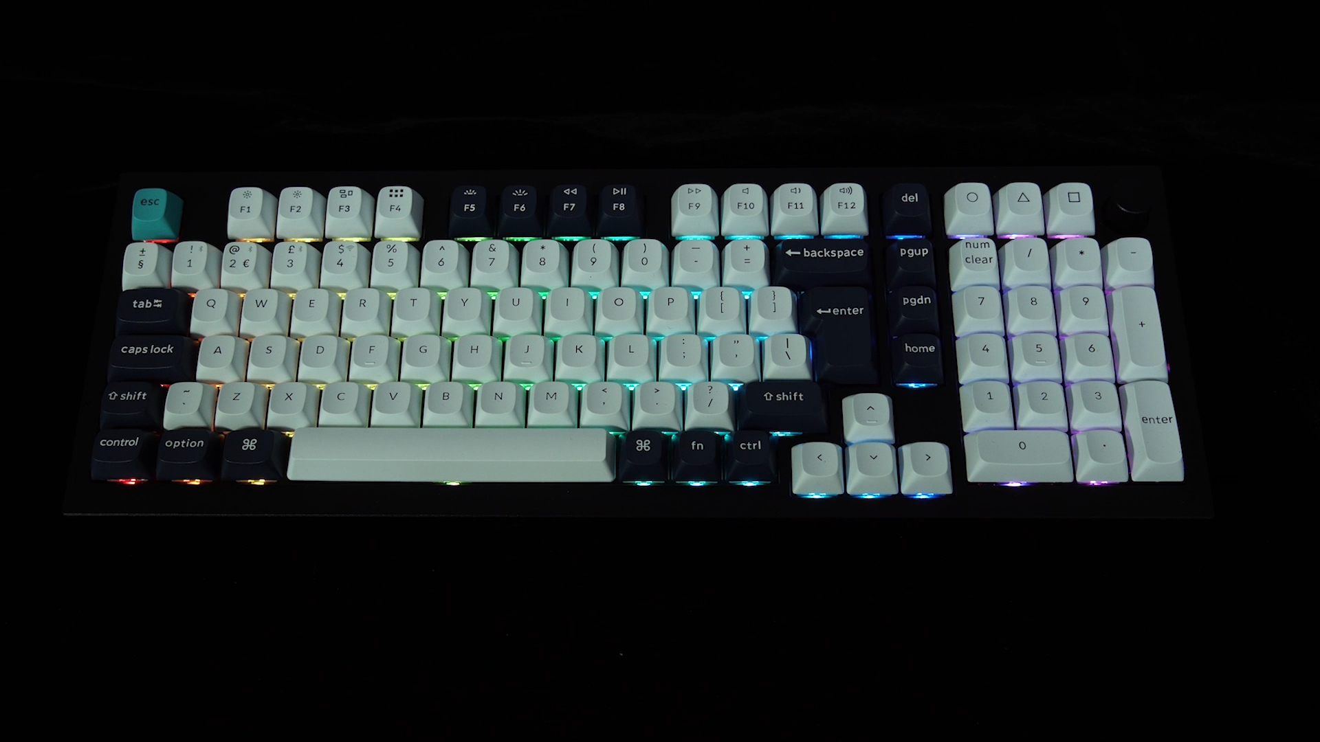 Eine Tastatur mit weißen Tasten und schwarzen Akzenten, beleuchtet von bunten Lichtern. Der Hintergrund ist schwarz.
