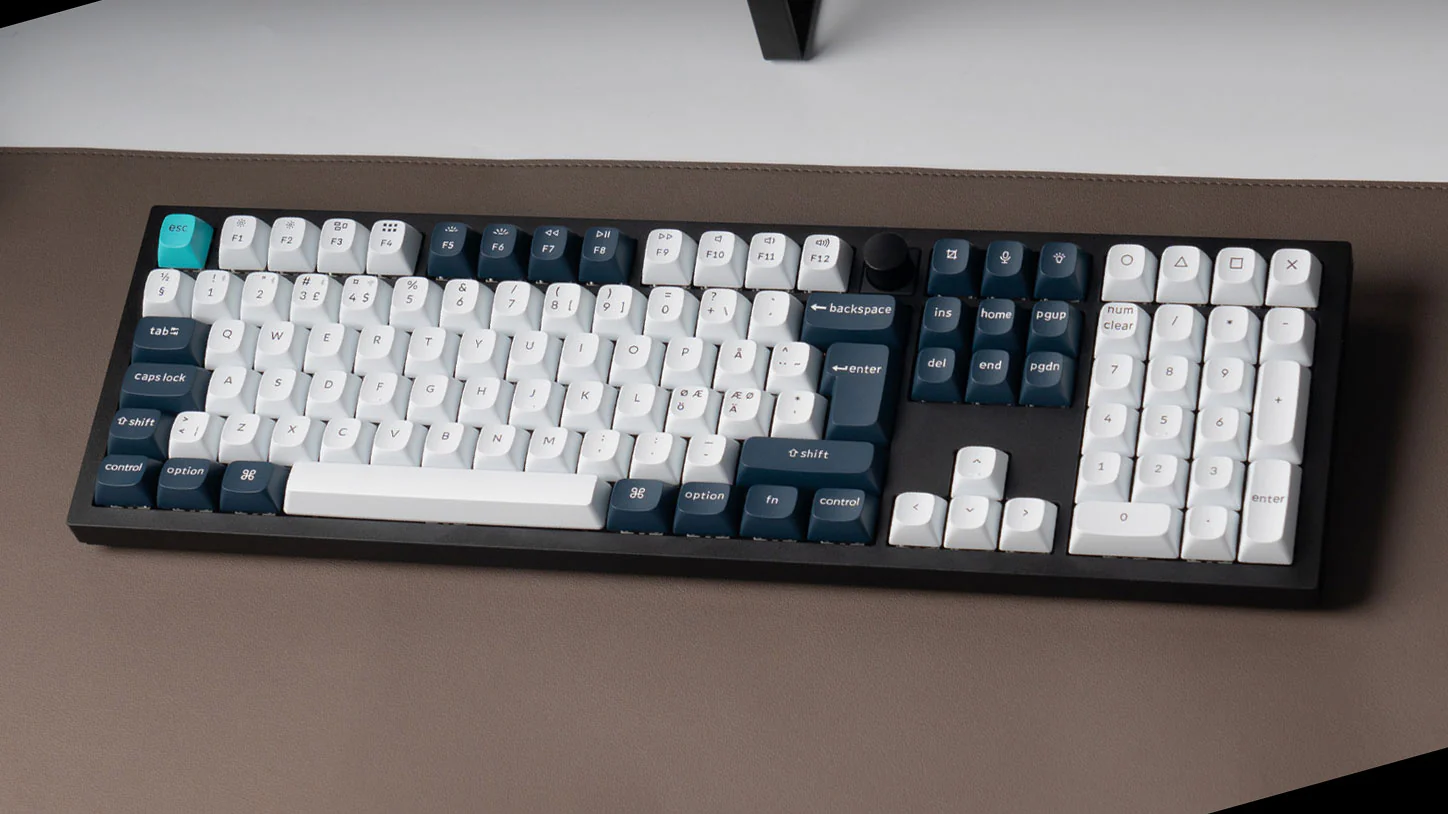 Eine schwarz-weiße mechanische Tastatur mit türkisfarbener Escape-Taste. Die Tastatur liegt auf einer braunen Oberfläche.