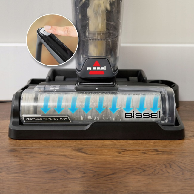 Podstawa odkurzacza z przezroczystą głowicą szczotkową. Palec naciska przycisk zasilania. Szczotka ma "ZEROGAP TECHNOLOGY".