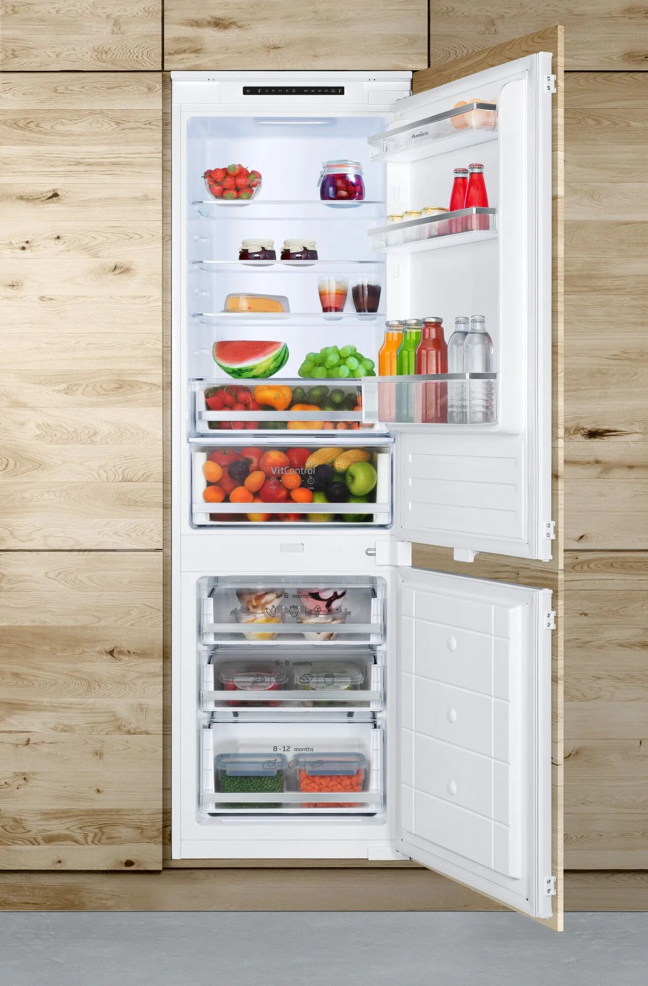 Otwarta lodówka wypełniona owocami, warzywami, sokami i dżemami. Drewniane panele po bokach. Drzwi są otwarte.