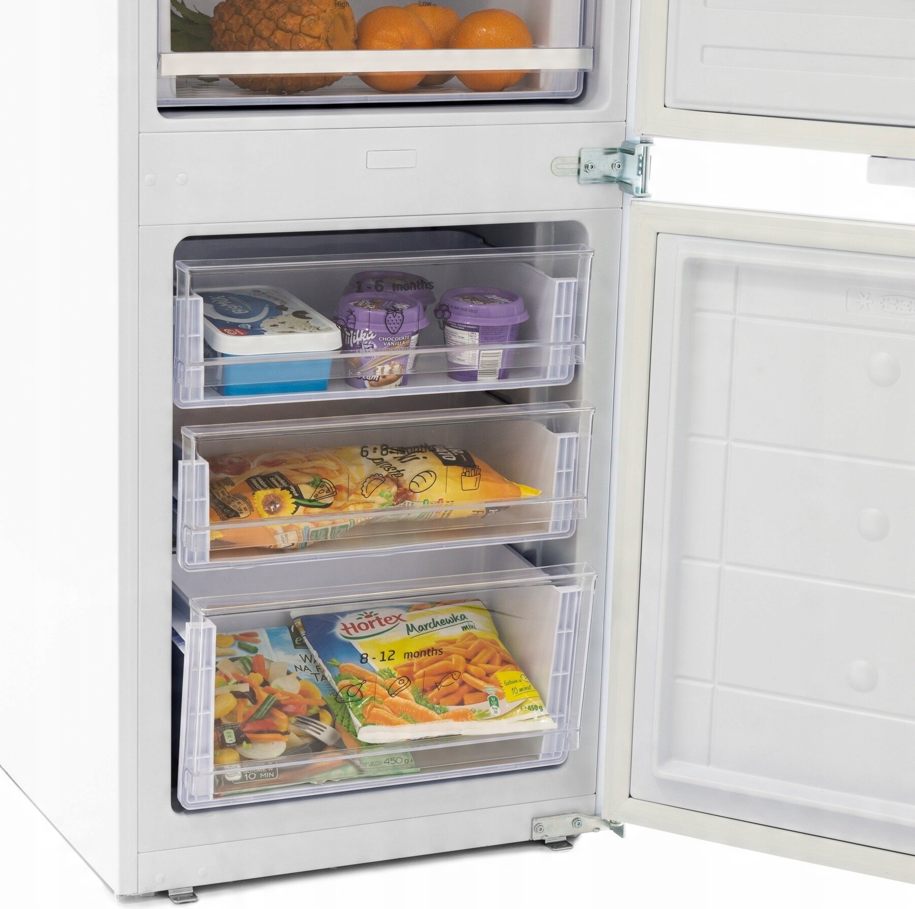 Lodówka z otwartymi drzwiami. Wewnątrz szuflady z mrożonkami, takimi jak warzywa, lody i owoce. Pomarańcze na górze.