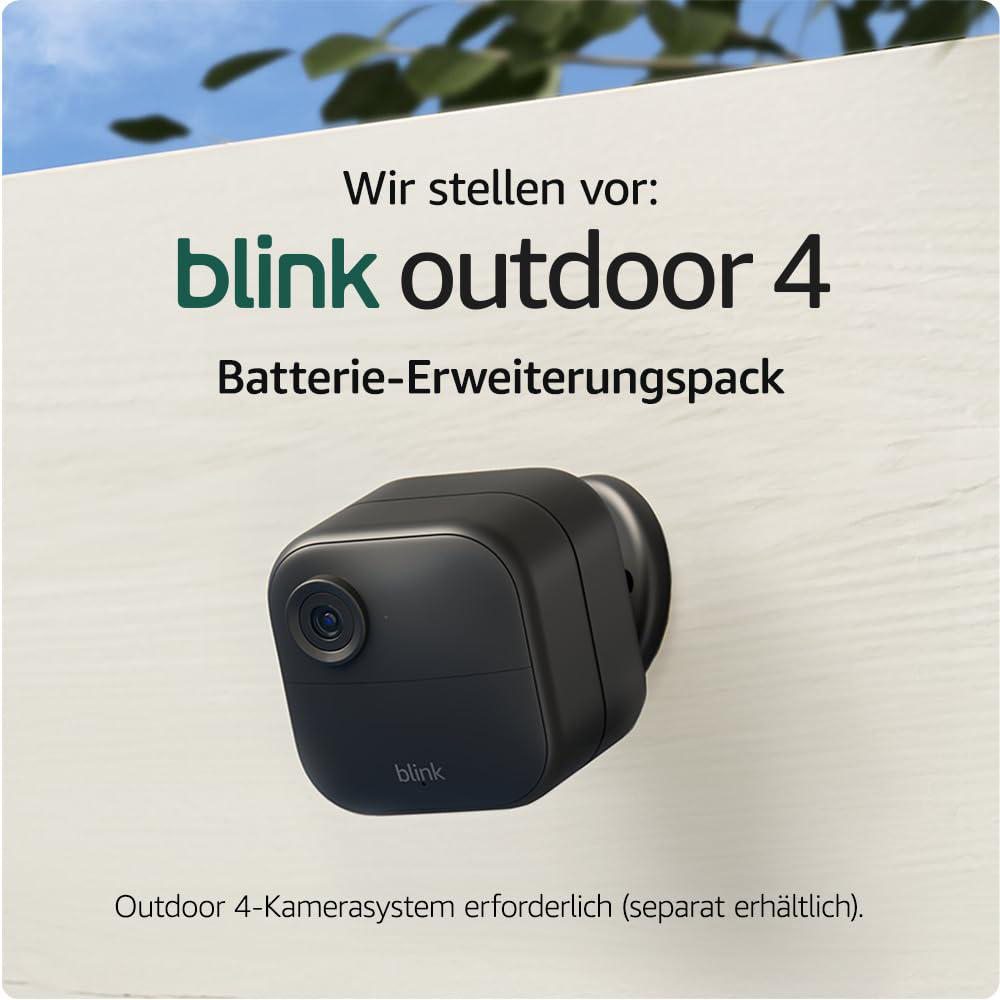 Schwarze Blink Outdoor 4 Kamera an einer weißen Wand, Text darüber lautet 'blink outdoor 4'. Grünes Laub im Hintergrund.