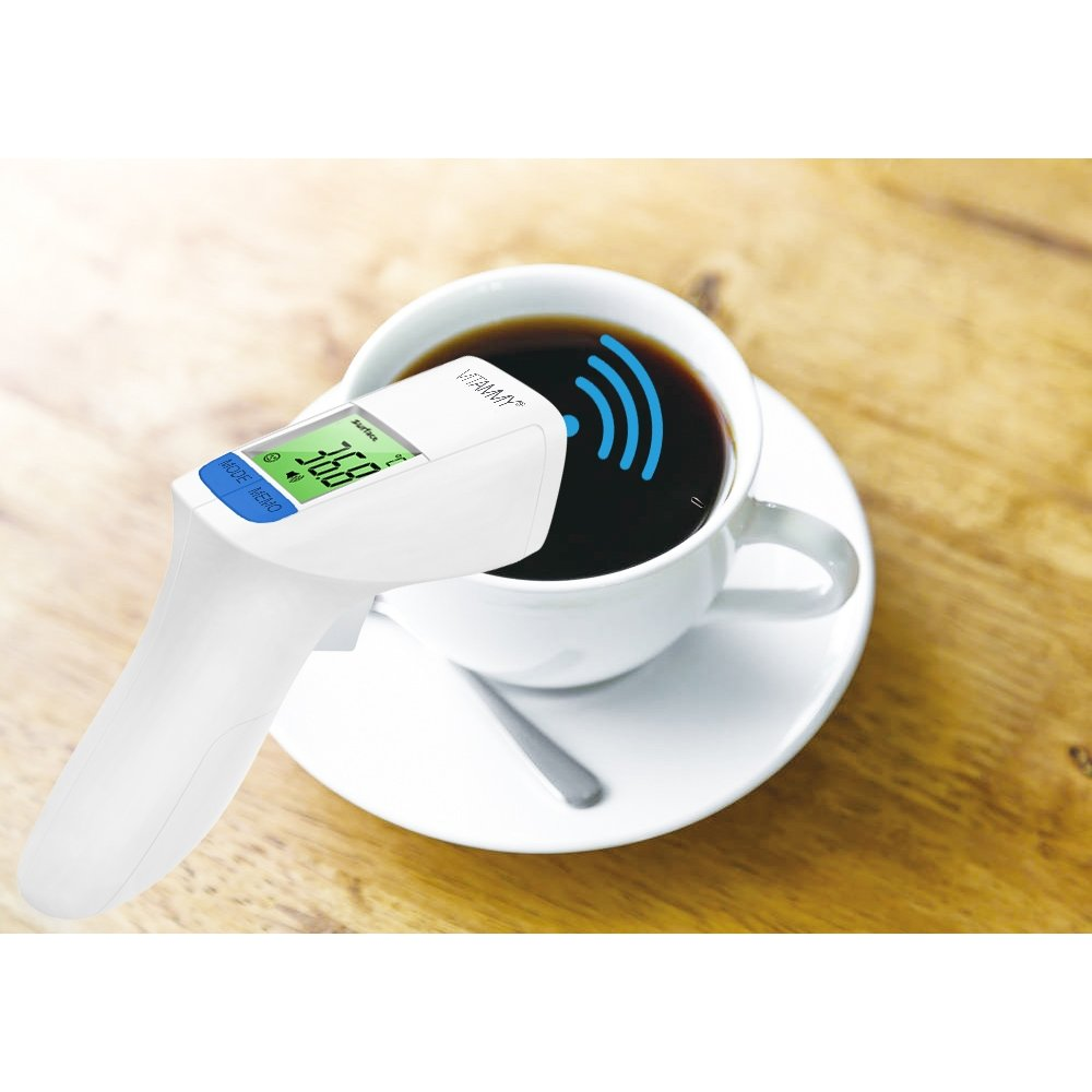 Biały termometr mierzy temperaturę kawy w białym kubku. Kubek stoi na spodku z łyżeczką na drewnianym stole.