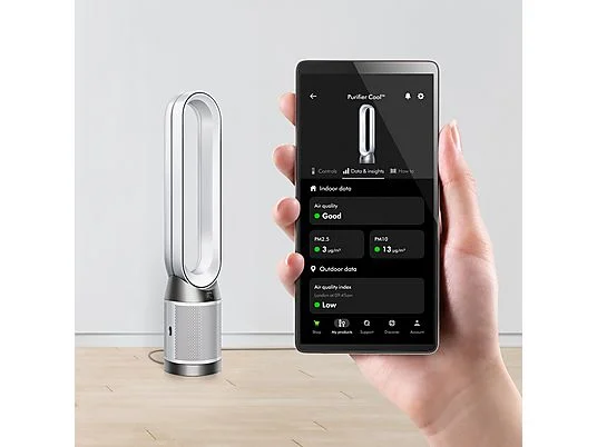 Una mano sostiene un teléfono que muestra datos de calidad del aire. Un purificador de aire Dyson está a su lado. El fondo es blanco.