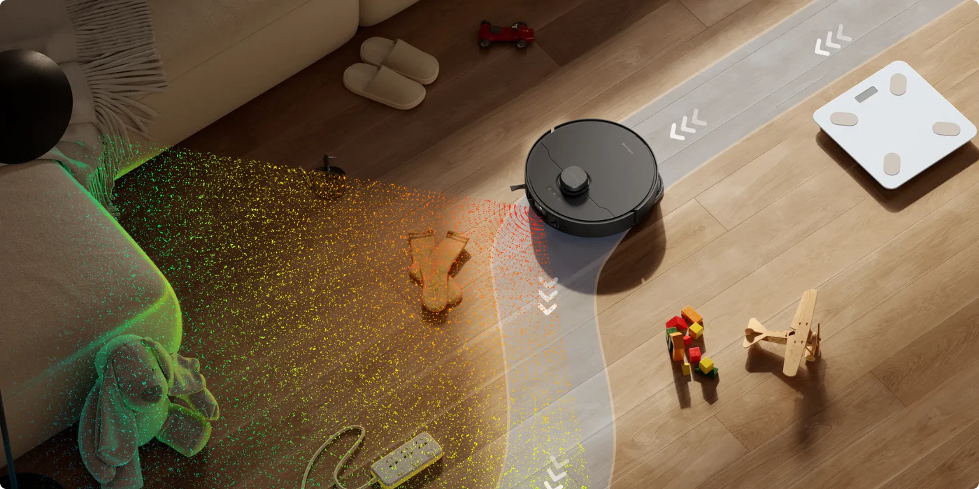 Robot porszívó takarít fapadlót. Játékok, zoknik, mérleg a padlón. Kanapé és fekete labda látható.