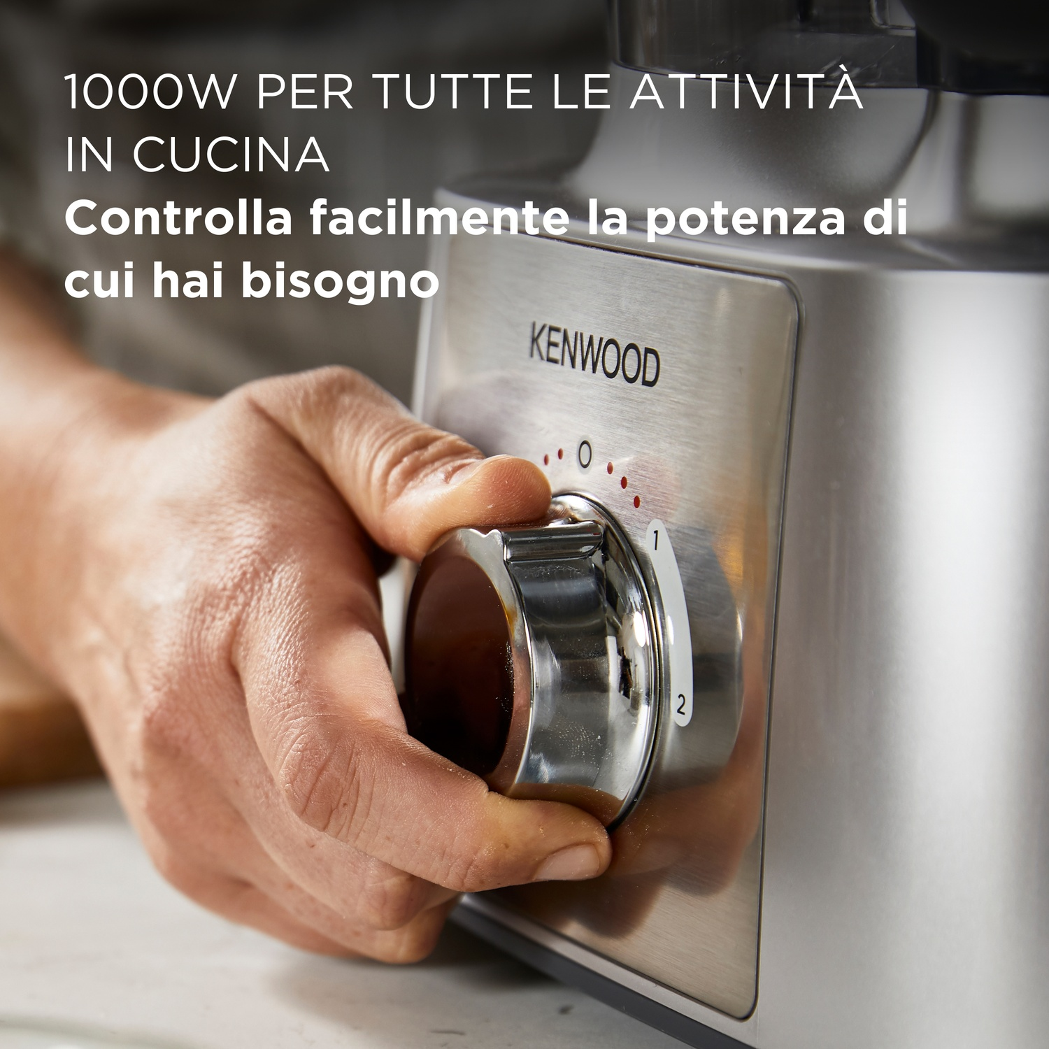 Una mano ruota una manopola su un robot da cucina Kenwood. La manopola è argentata con numeri. Il testo dice: "1000W per tutte le attività in cucina".