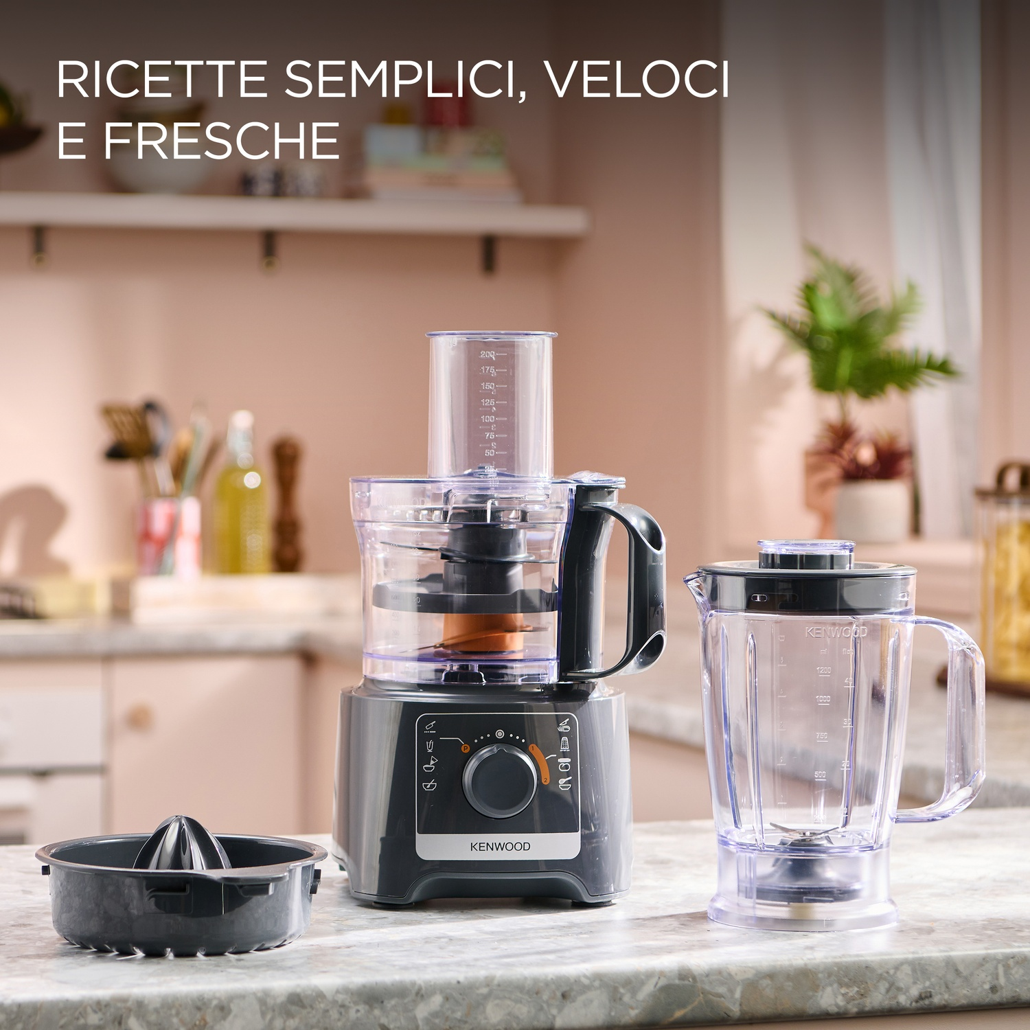 Un robot da cucina e un frullatore su un bancone. Un accessorio spremiagrumi è appoggiato davanti. Lo sfondo è una cucina con piante e scaffali.