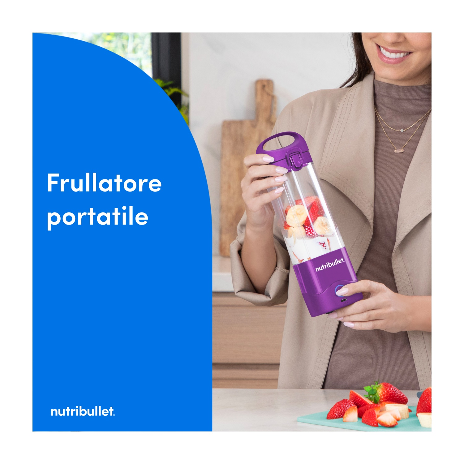 Una donna tiene in mano un Nutribullet viola con dentro della frutta. Fragole e banane a fette sono su un tagliere.