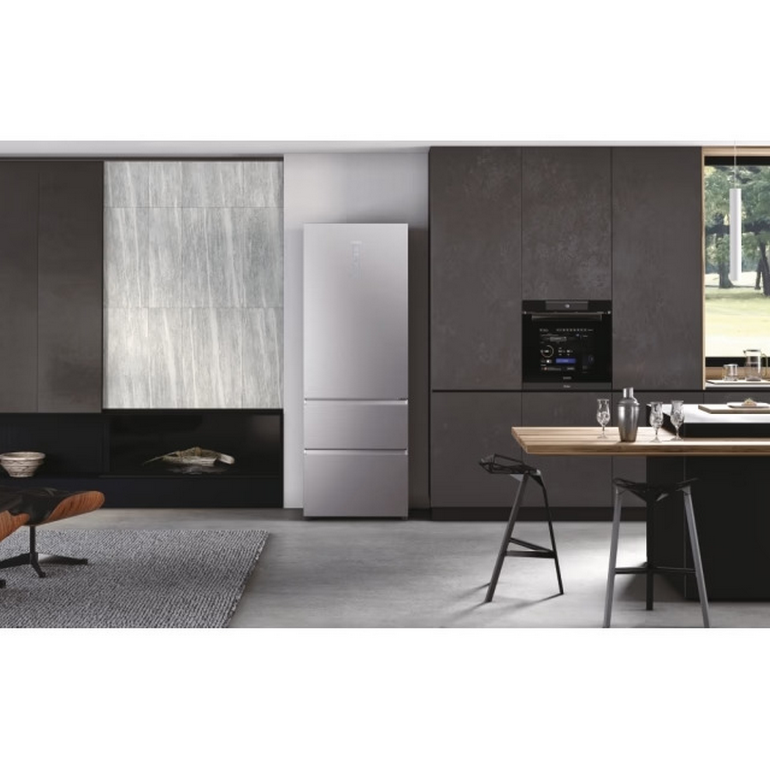 Cocina moderna con nevera de acero inoxidable, armarios oscuros, mesa de madera y dos taburetes. Una ventana muestra árboles.