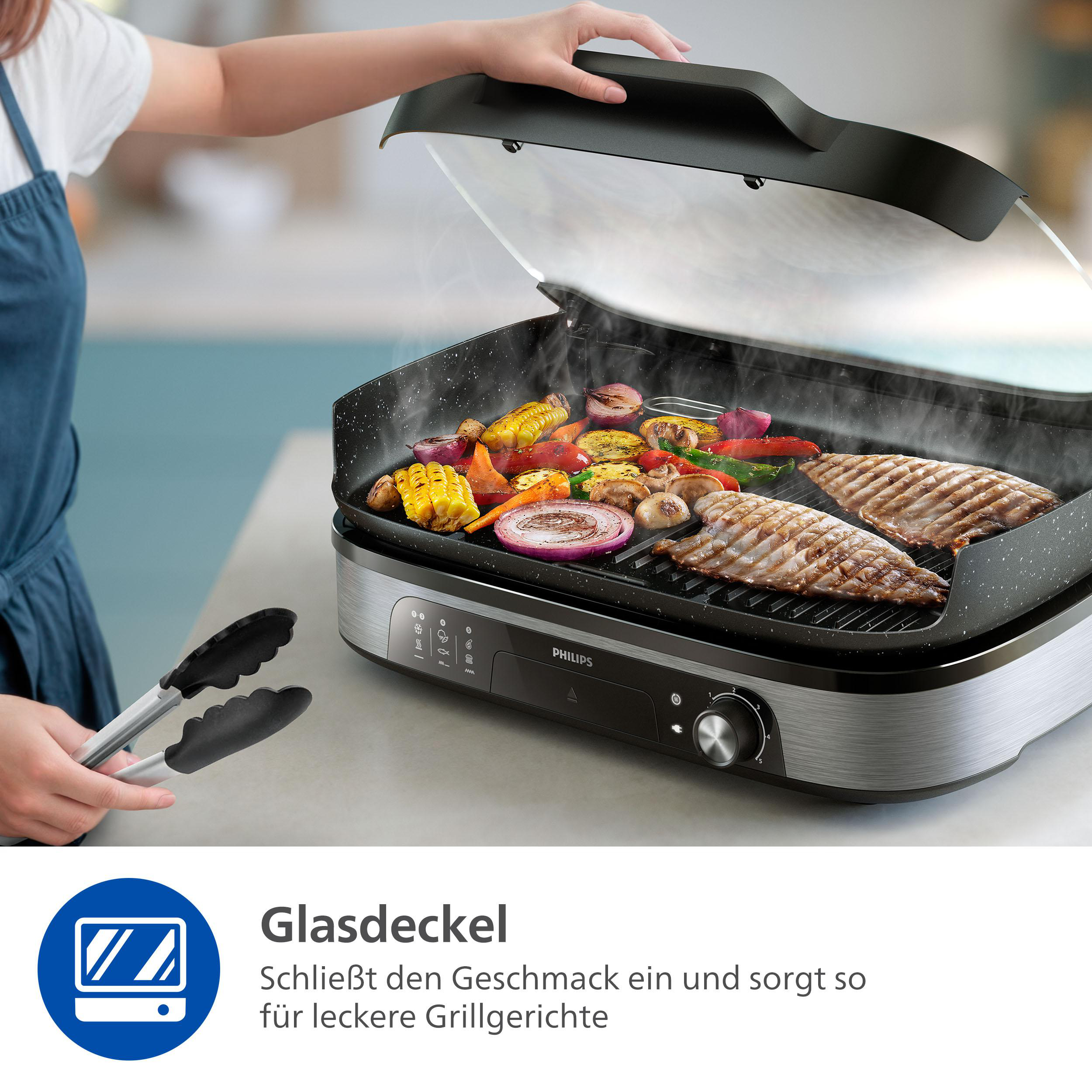 Grill mit Gemüse und Fisch, Deckel offen. Eine Person hält eine Zange. Philips-Logo sichtbar.