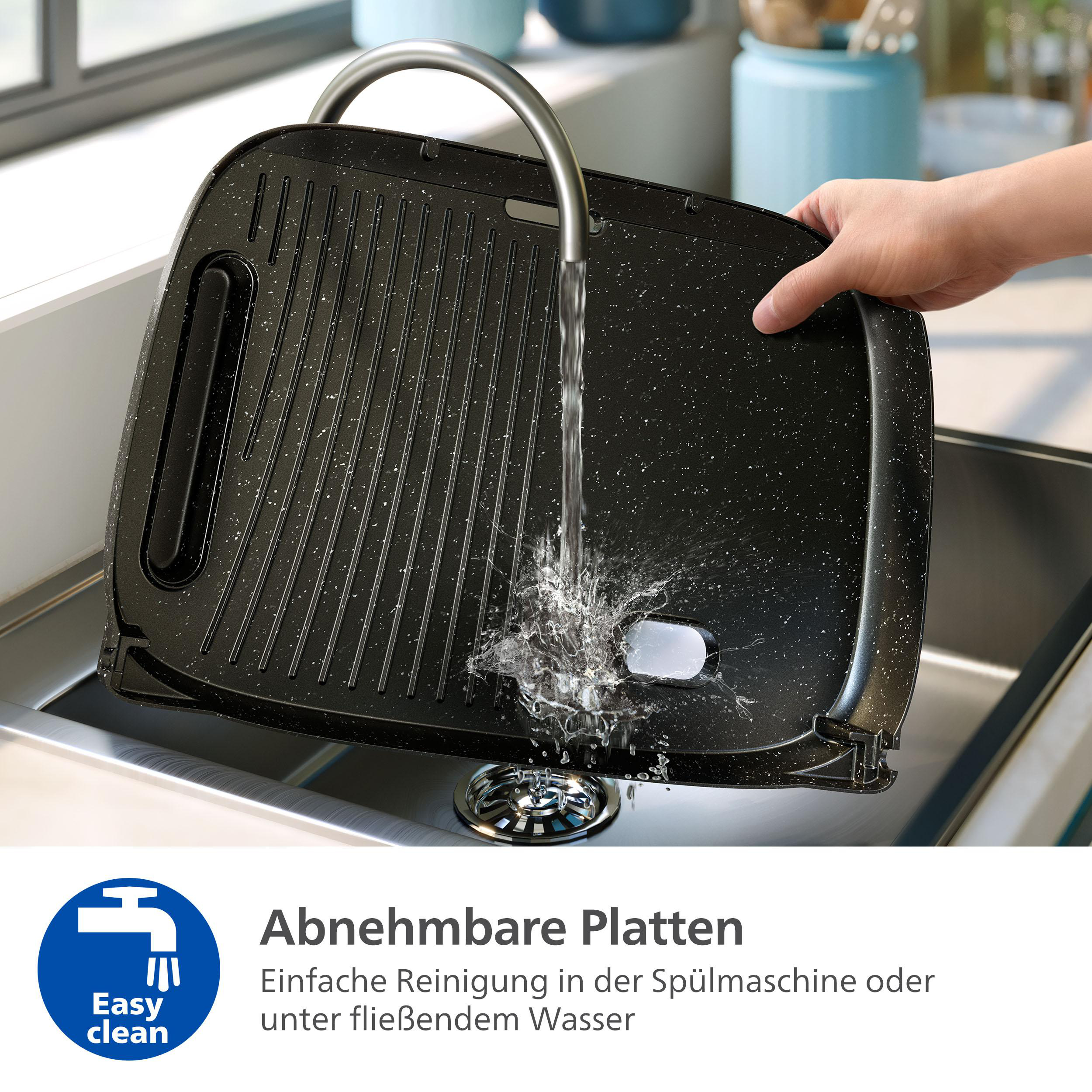 Eine schwarze Grillpfanne wird unter einem Wasserhahn in einem Küchenbecken gespült. Wasser spritzt auf die Pfanne.