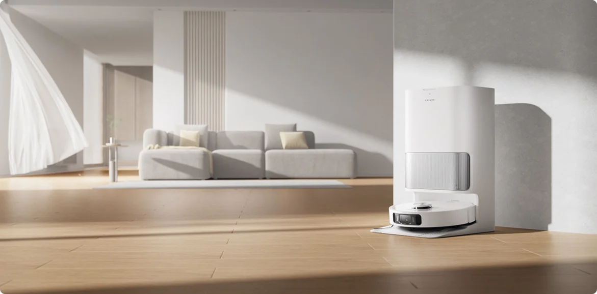 Egy fehér robotporszívó és az állomása egy modern nappaliban. Egy kanapé és egy függöny látható.